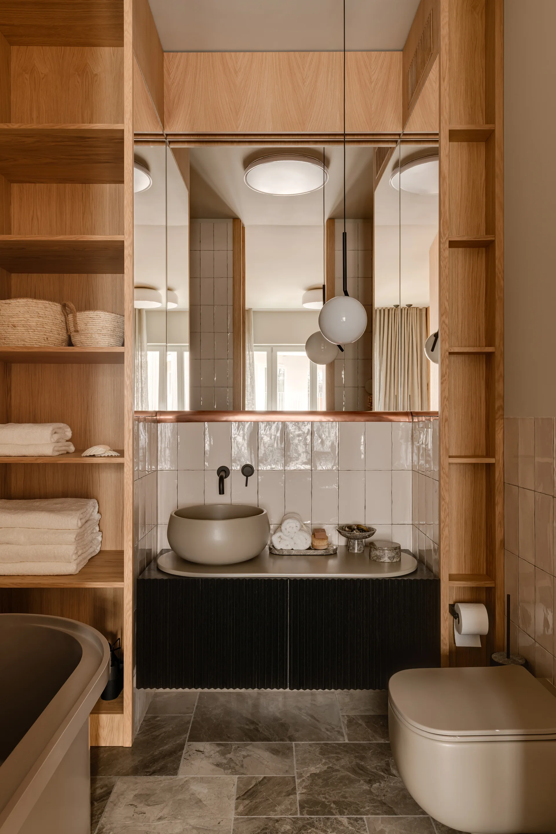 A modern bathroom featuring a dark fluted vanity with a vessel sink, built-in light wood shelving, and glossy square wall tiles.