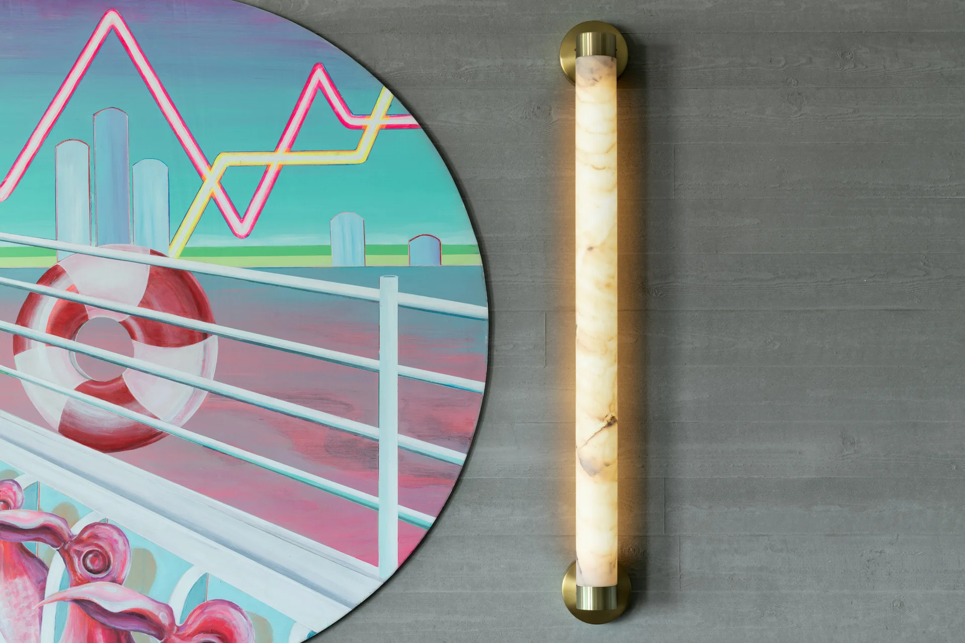 A vertical, glowing cylindrical stone wall sconce with brass fittings mounts to a textured grey concrete wall next to a circular graphic painting.