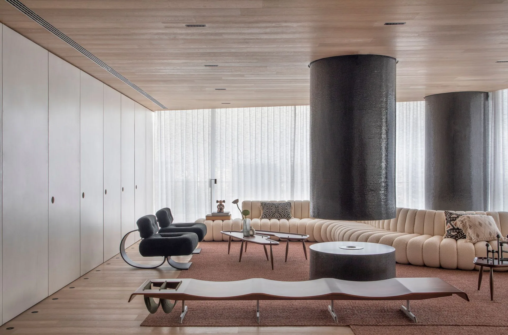 A contemporary living room features a suspended circular black fireplace, a curved cream sectional sofa, and wood-paneled ceiling and floors.