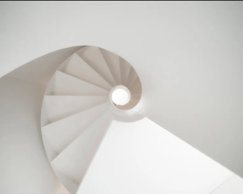A high-angle view of a smooth white spiral staircase showcasing clean geometric curves and a bright central light well.