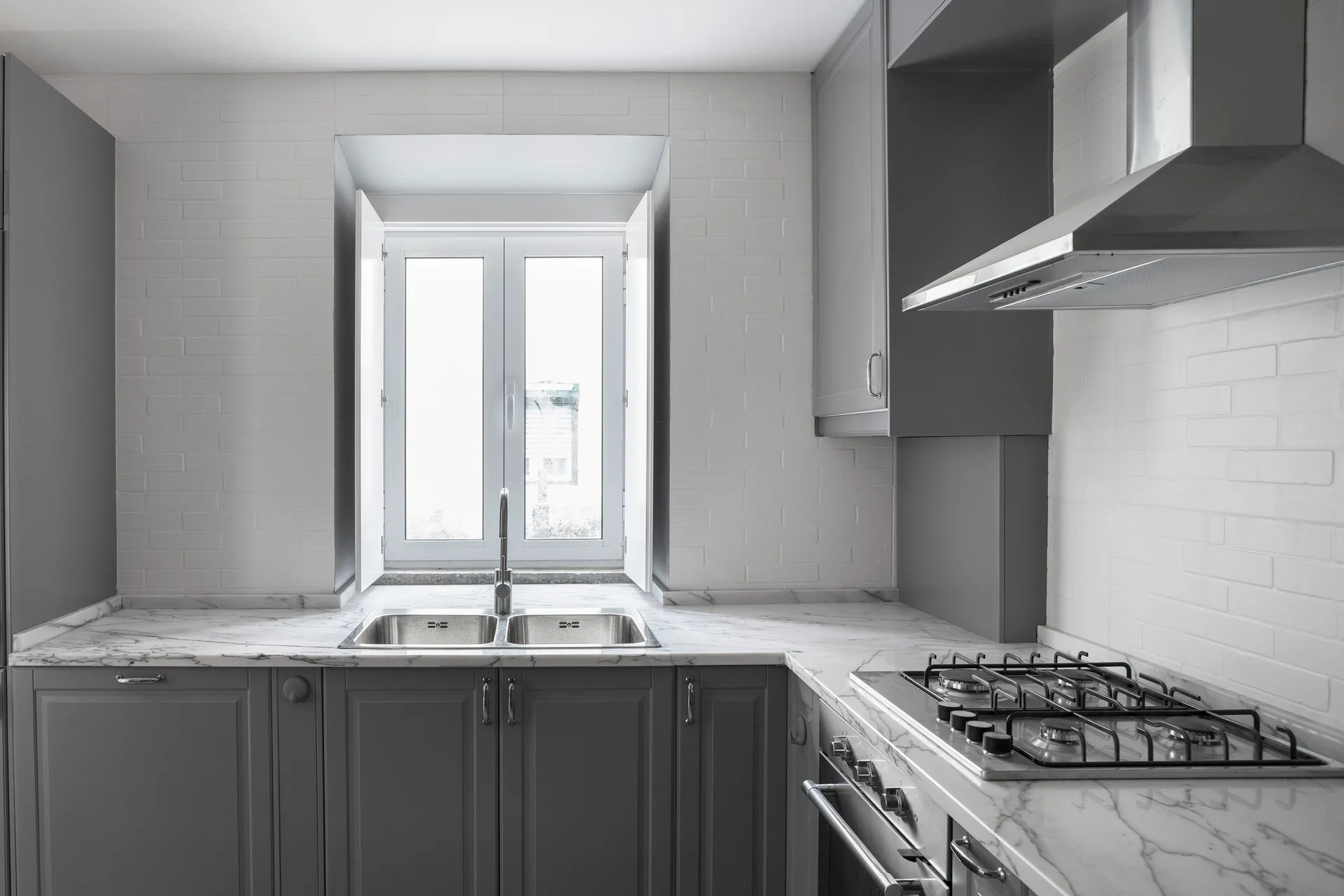 A kitchen features dark gray shaker cabinets, white veined marble countertops, a double undermount sink, and a white brick tile backsplash.