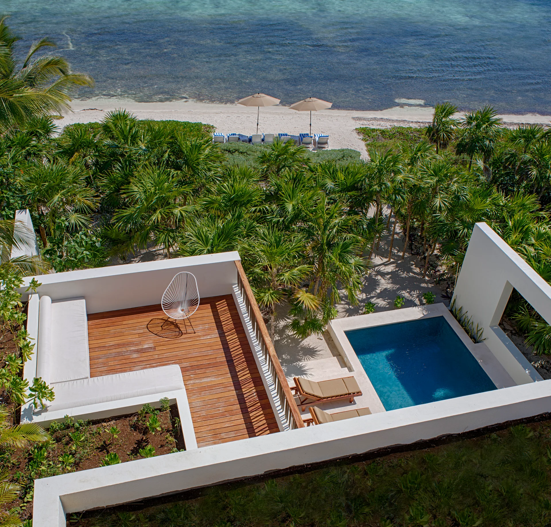 An aerial view of a modern terrace featuring wood decking, a built-in white corner bench, a small plunge pool, and ocean views.