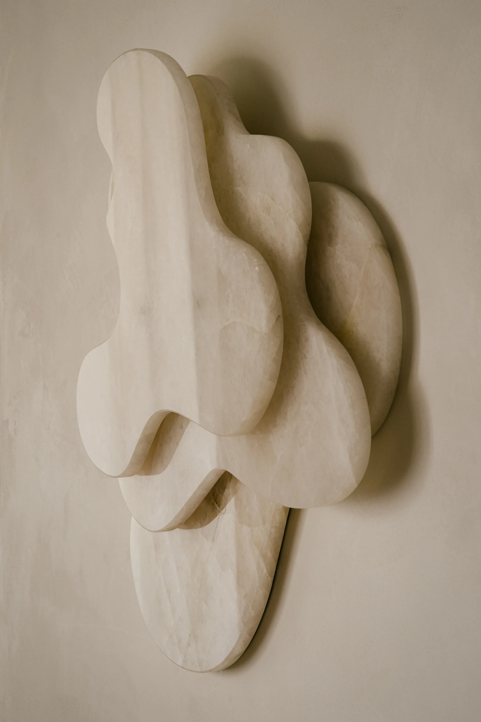 An abstract layered wall sculpture crafted from organic beige stone panels is mounted on a smooth plaster wall under soft directional light.