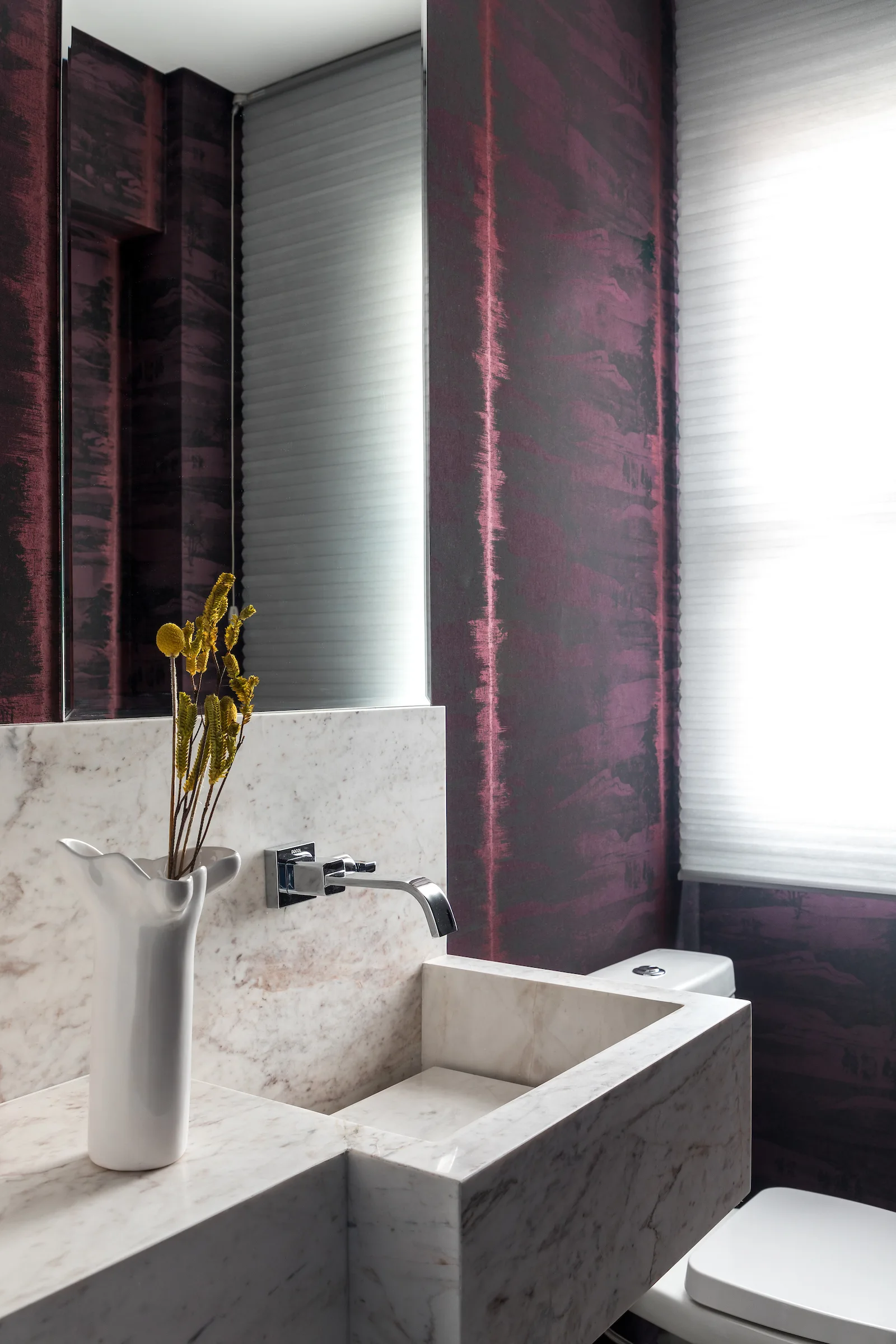 A powder room features textured purple wallpaper, an integrated marble sink with a wall-mounted faucet, and a white ceramic vase with yellow flowers.