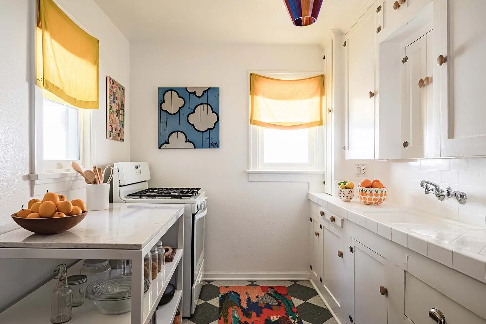 A bright white galley kitchen features a grey and white checkerboard floor, yellow window shades, and a white gas stove.