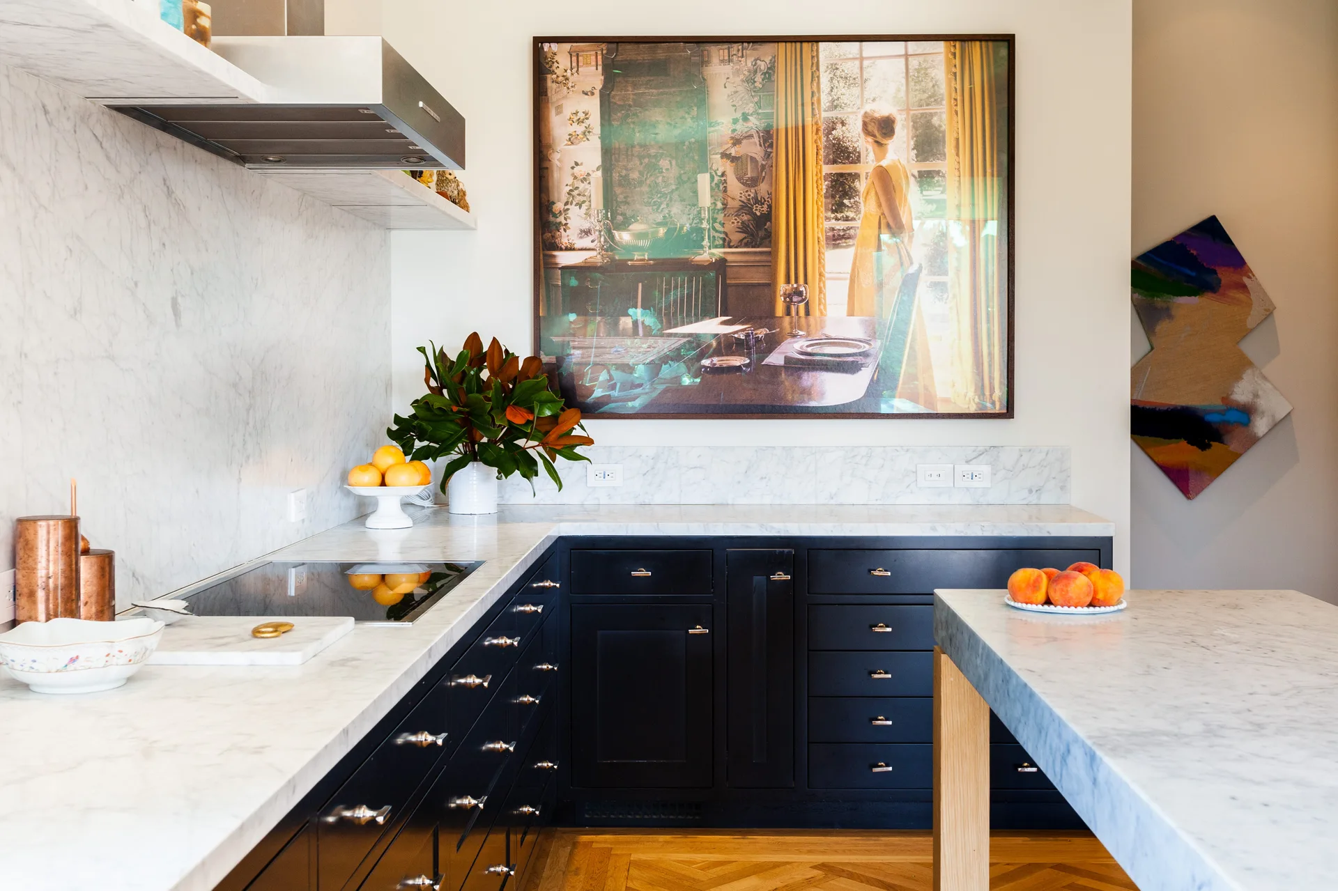 A modern kitchen featuring dark blue base cabinetry, white veined marble countertops, a matching backsplash, and a large framed painting on the wall.
