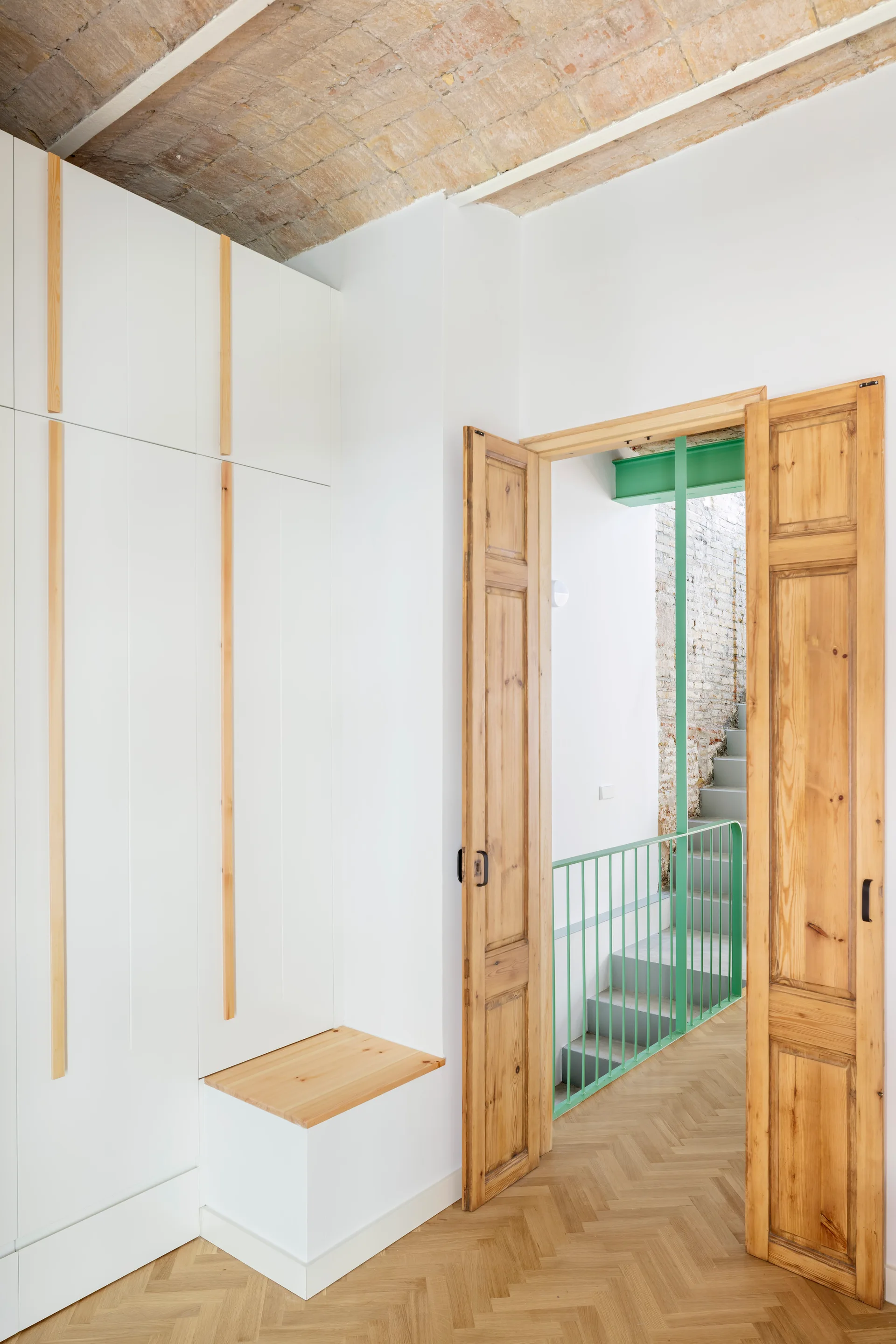 A bright entryway features tall white built-in closets with wood handles, a herringbone wood floor, and wooden doors opening to a staircase.
