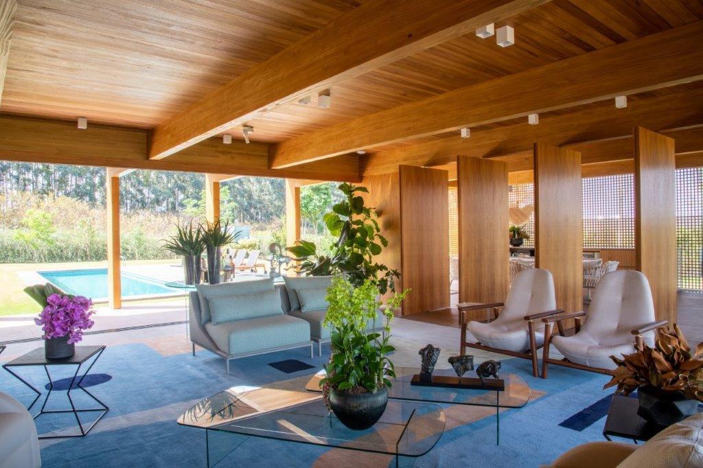 A modern open-plan living room with a wood ceiling, wood partition walls, a blue rug, and large sliding doors looking out to a pool.