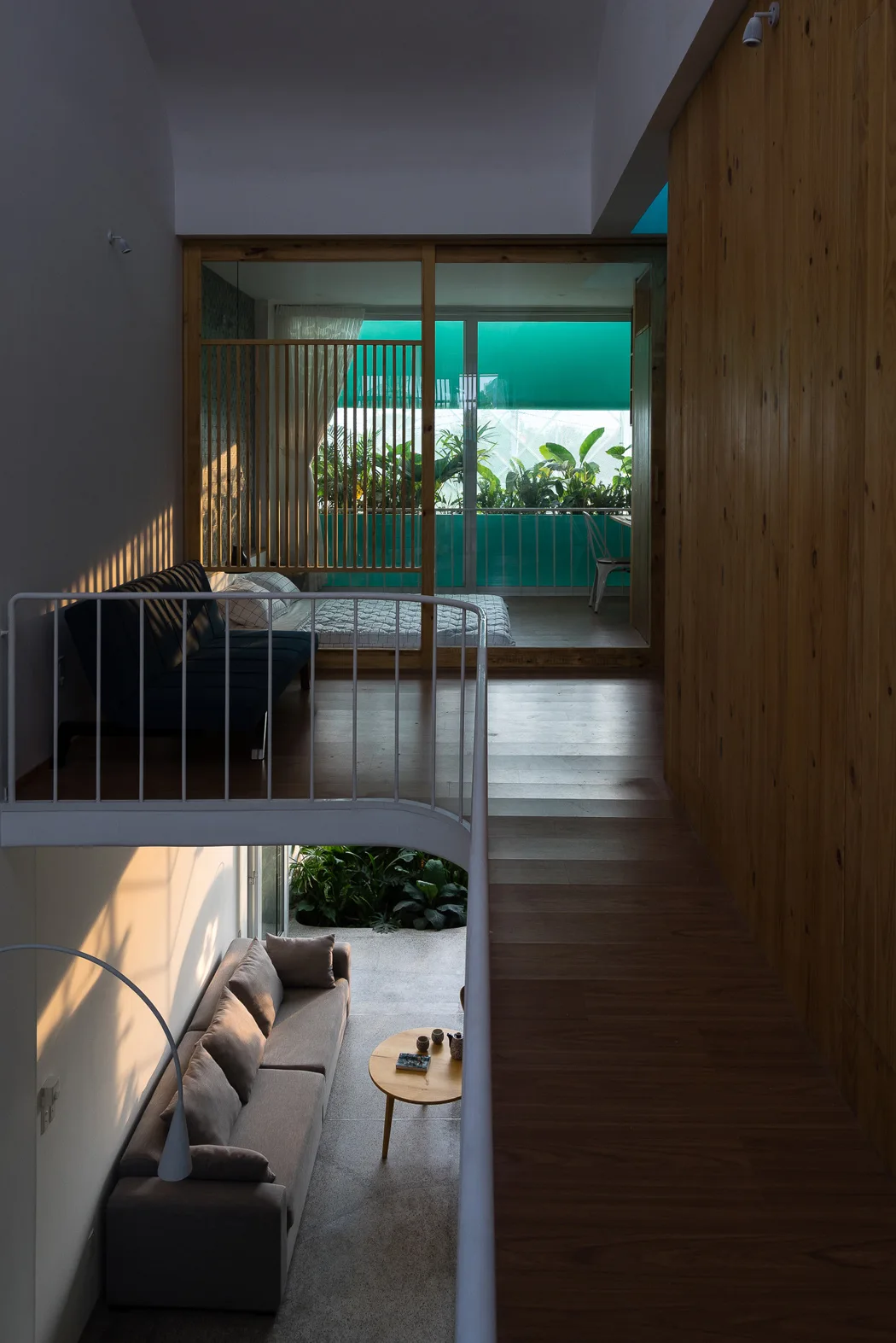 Looking down from a mezzanine walkway with a white metal railing to a lower living area with a grey sofa and coffee table.