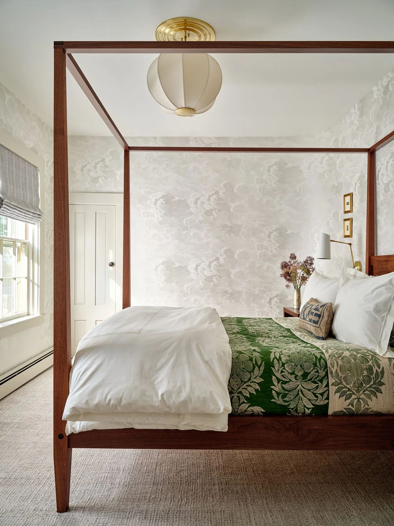 A bedroom features a dark wood canopy bed with white and green bedding against walls covered in cloud-patterned wallpaper.