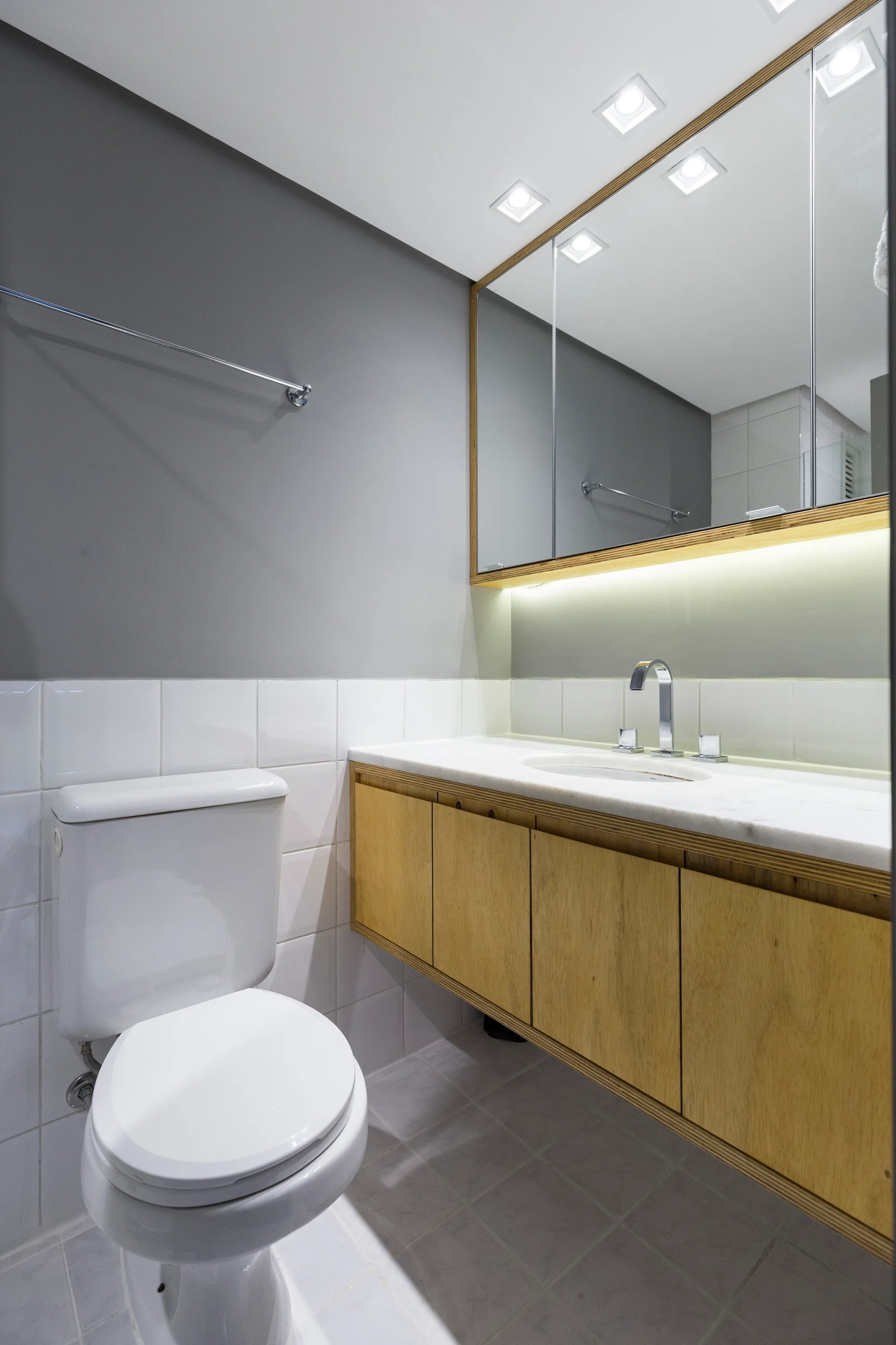 A modern bathroom featuring a floating wood vanity with white countertop, white square wall tiles, a white toilet, and a large mirrored medicine cabinet.