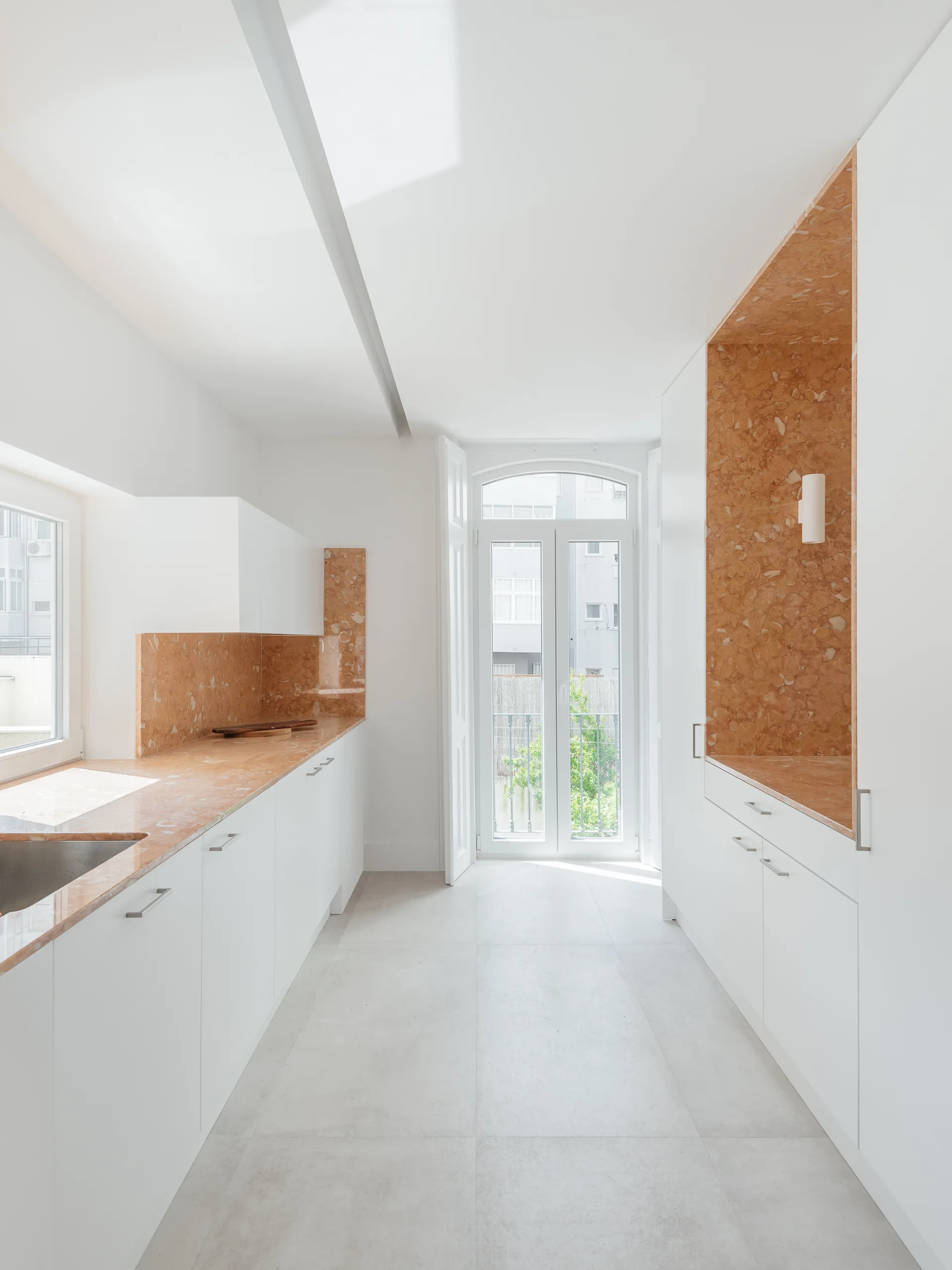 A minimalist white galley kitchen features patterned orange stone countertops, a matching tall niche, and an arched glass door.