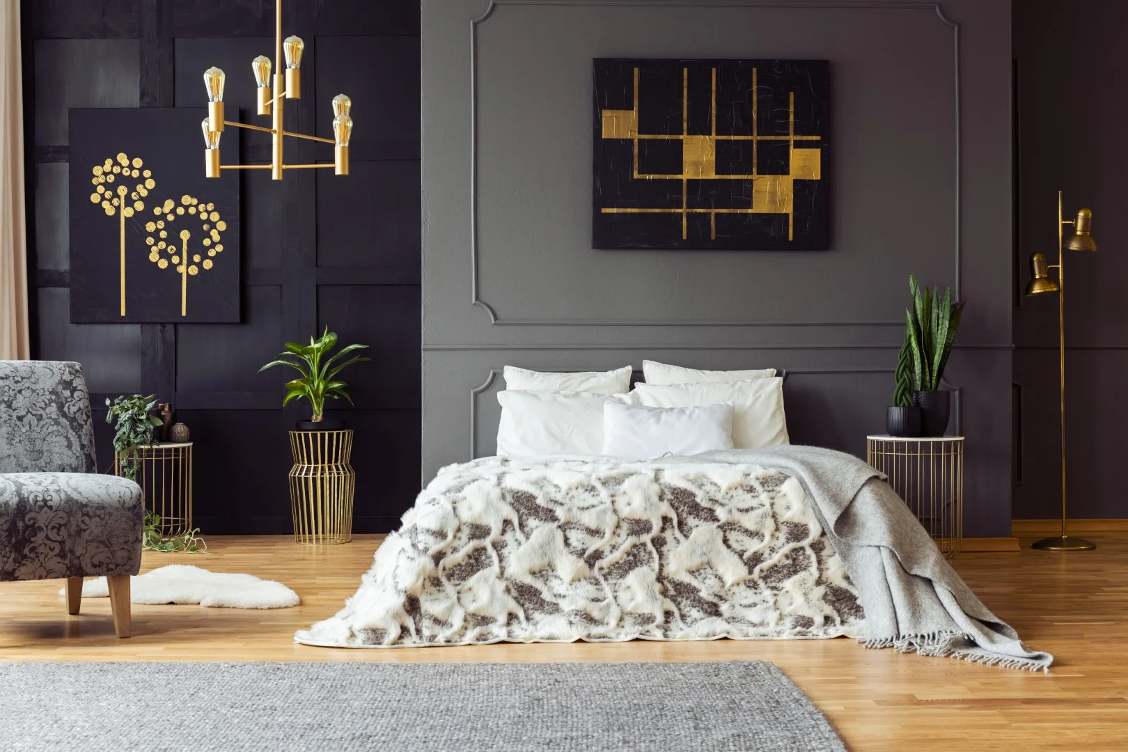 A bedroom with dark gray paneled walls, a bed with a faux-fur blanket, gold wire nightstands, and a brass chandelier.
