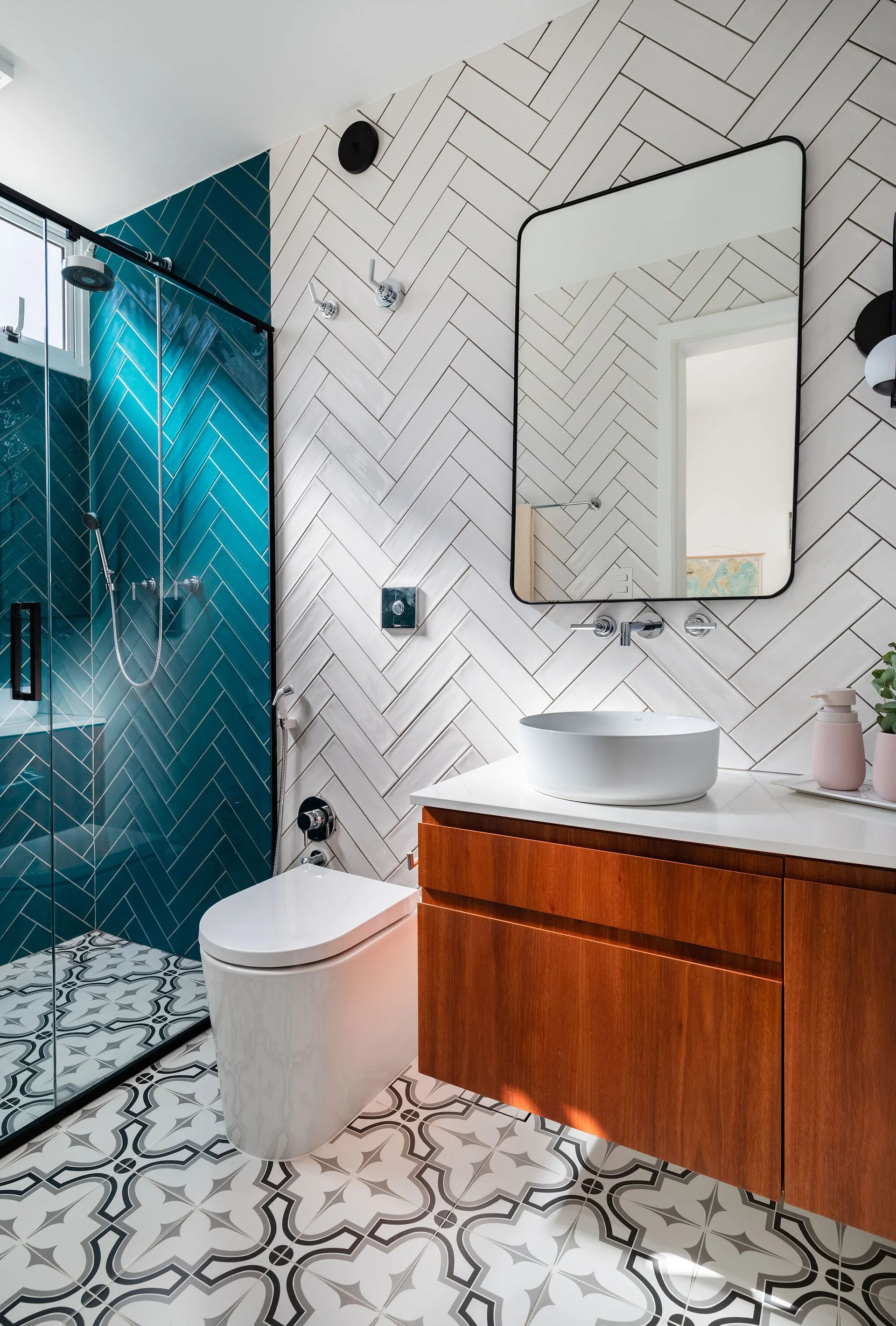 A bathroom features a teal and white herringbone tile wall, a floating wood vanity with a white vessel sink, and geometric patterned floor tiles.