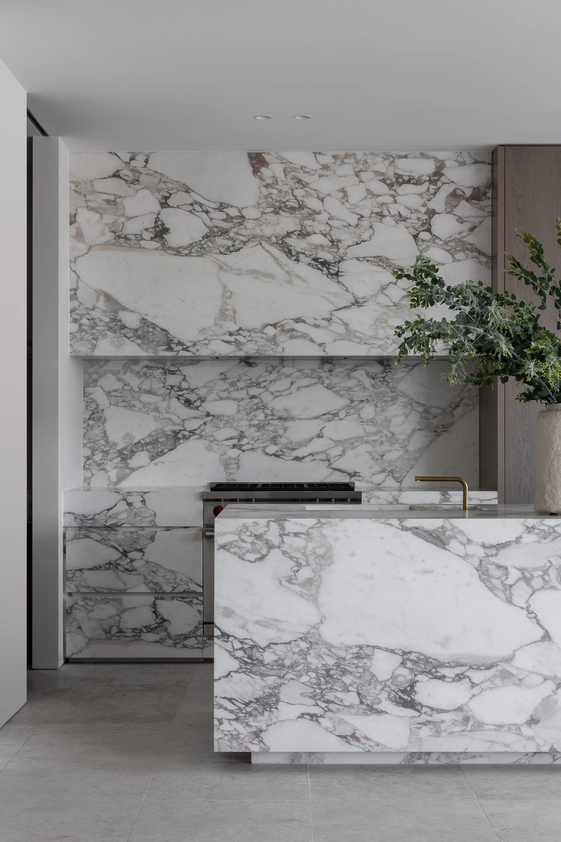 A modern kitchen featuring matching veined white and grey marble surfaces on the island, backsplash, and cabinet fronts alongside integrated appliances.