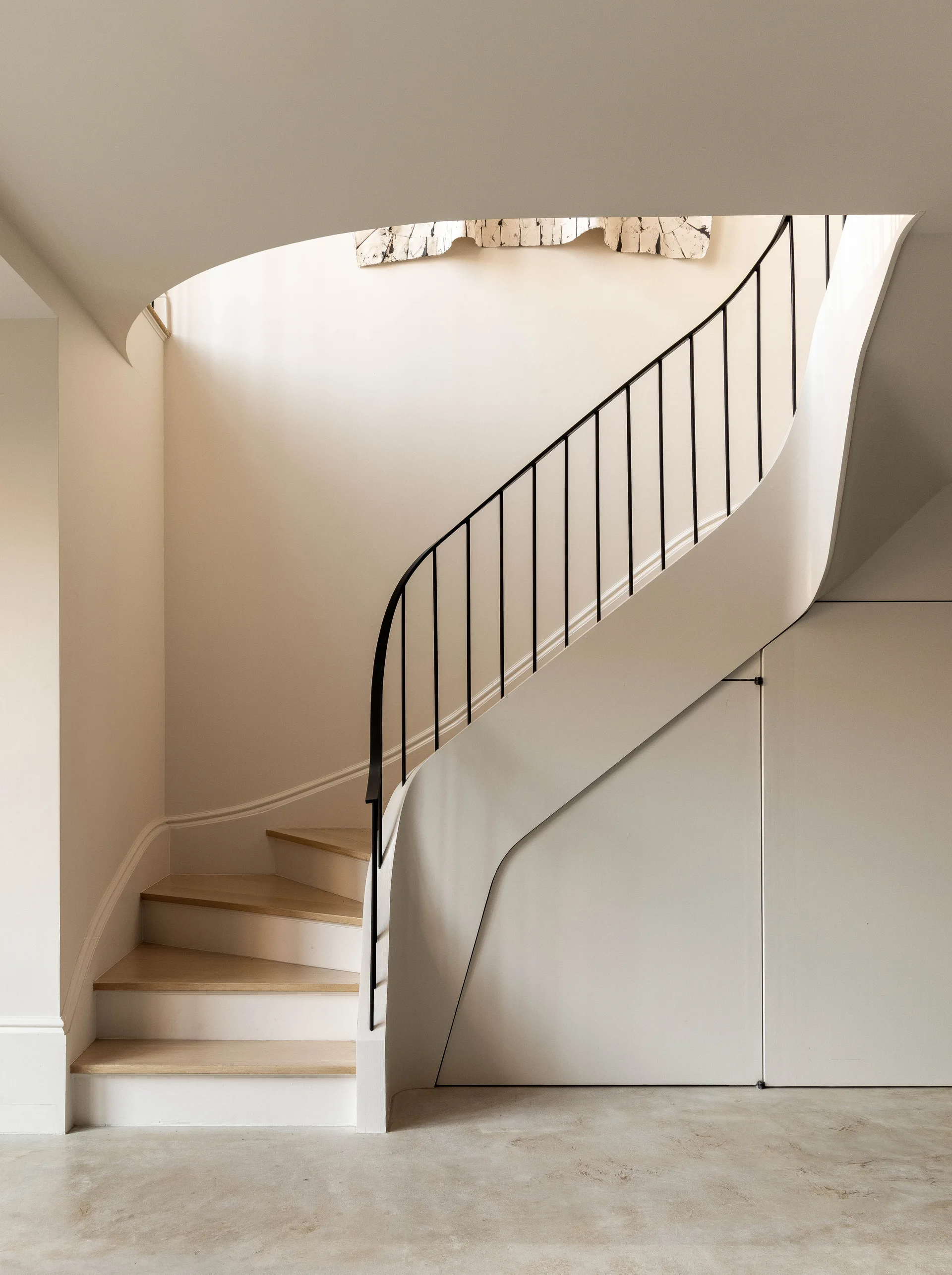 A curved modern staircase with light wood treads and a black metal railing features seamless under-stair storage doors.