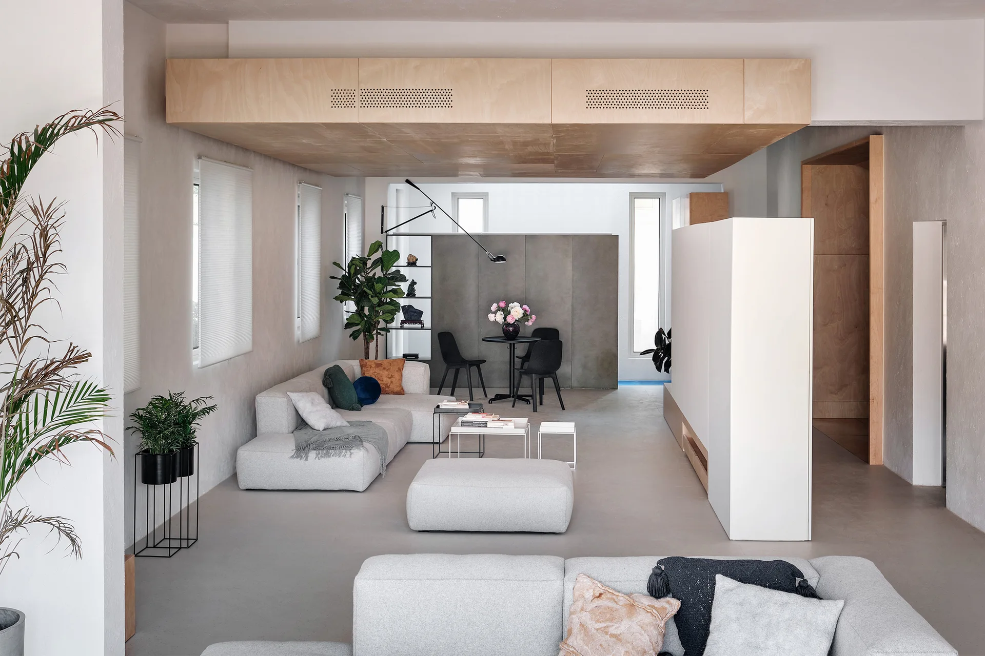 A minimalist living room featuring grey modular sofas, a large natural wood ceiling soffit, and a white freestanding partition wall.