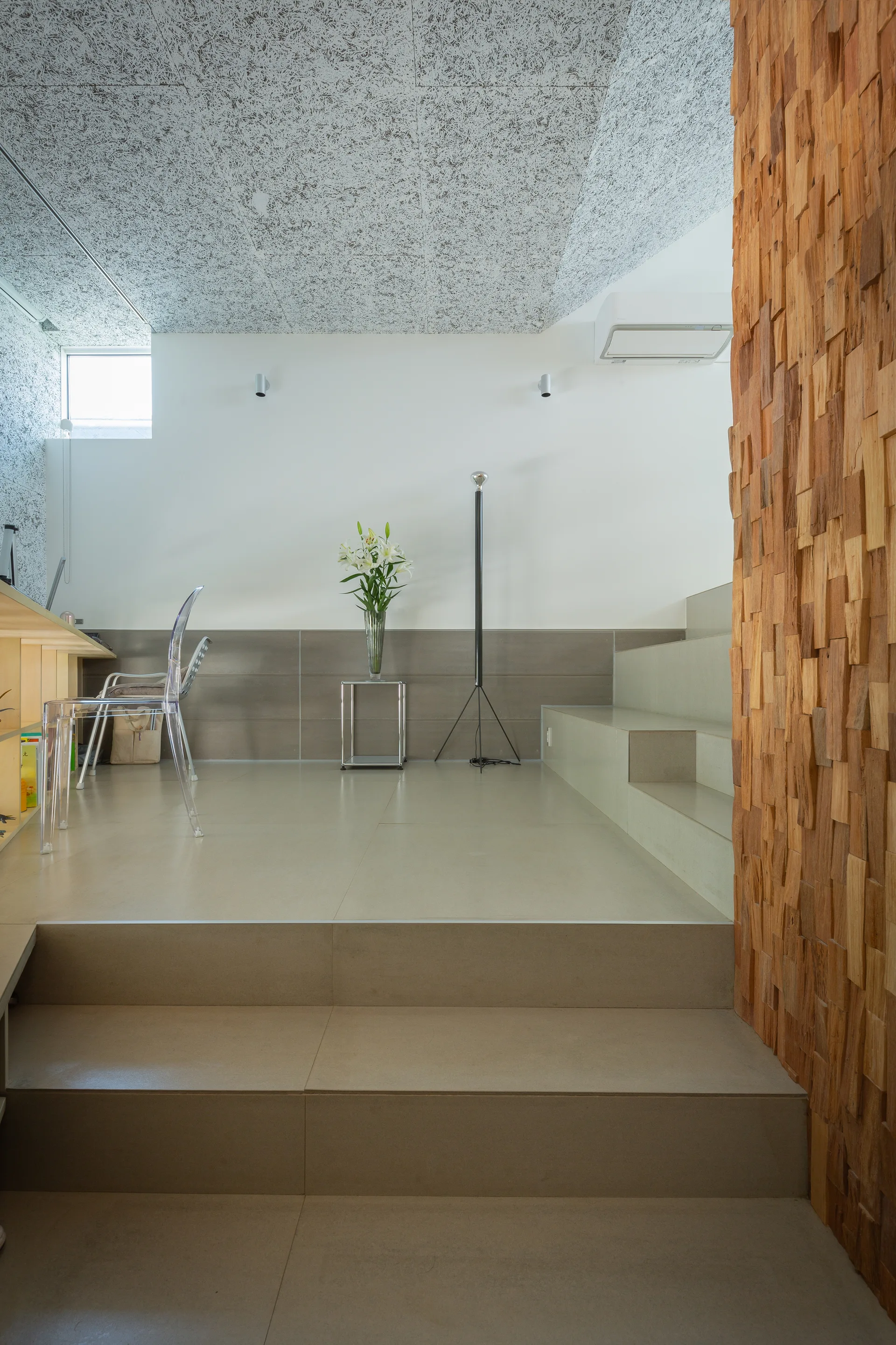 Modern split-level interior featuring beige tiled steps, a textured wood block accent wall, and a transparent acrylic chair.