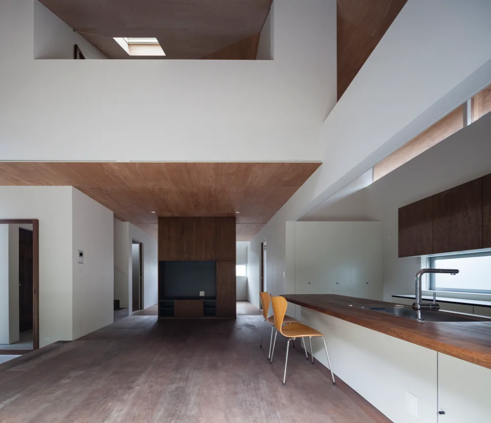 A modern kitchen features a warm wood-paneled ceiling, a long wooden island with an integrated sink, two wooden barstools, and white walls.