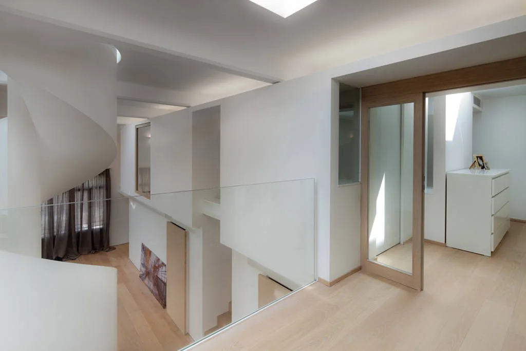 A modern minimalist landing features light wood floors, a white spiral staircase, a glass railing, and a wooden-framed glass sliding door.