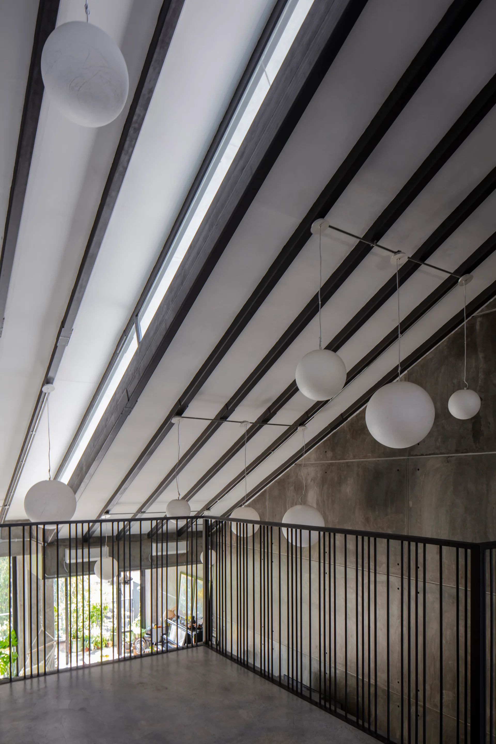 An industrial loft landing with a sloped beamed ceiling, hanging white globe pendant lights, and an exposed concrete wall.