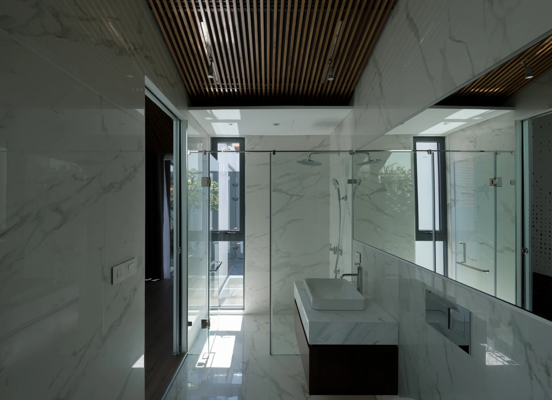 A contemporary bathroom clad in polished white veined marble, featuring a glass shower, floating vanity, and a slatted dark wood ceiling.