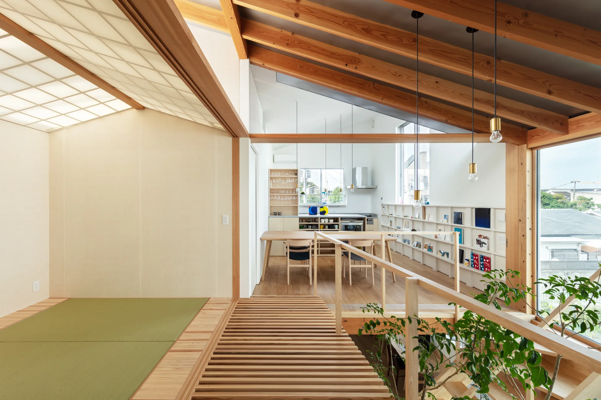 An open-plan residential interior featuring a tatami room in the foreground transitioning to a wood-beamed dining area and kitchen.