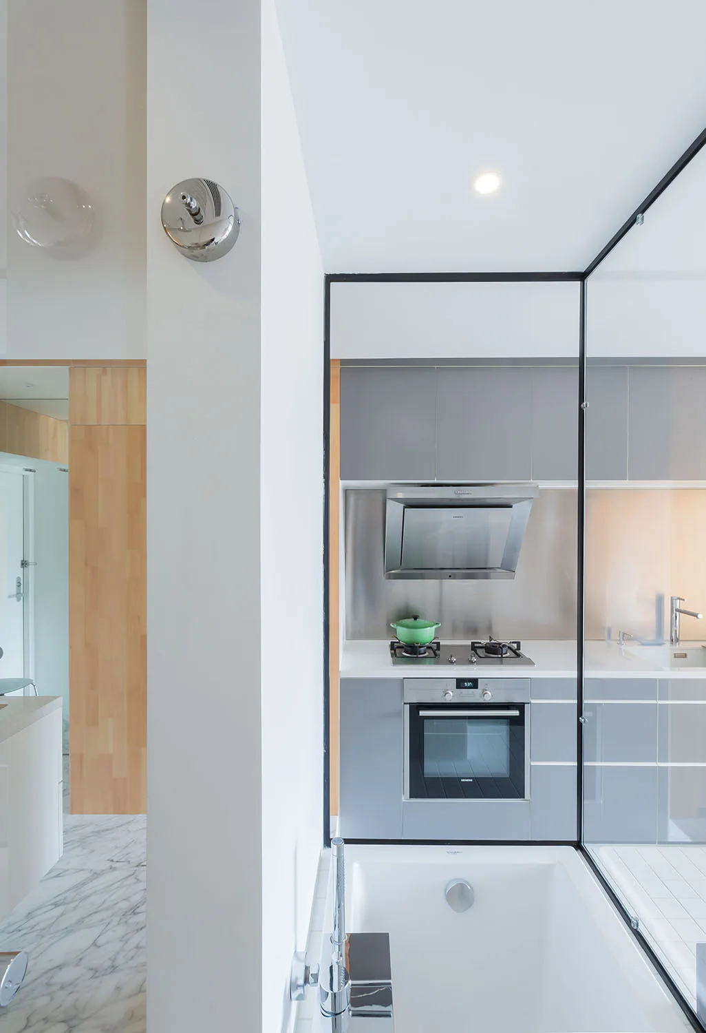 A modern compact grey kitchen with a stainless steel stove separated from a white bathtub by a black-framed glass partition.