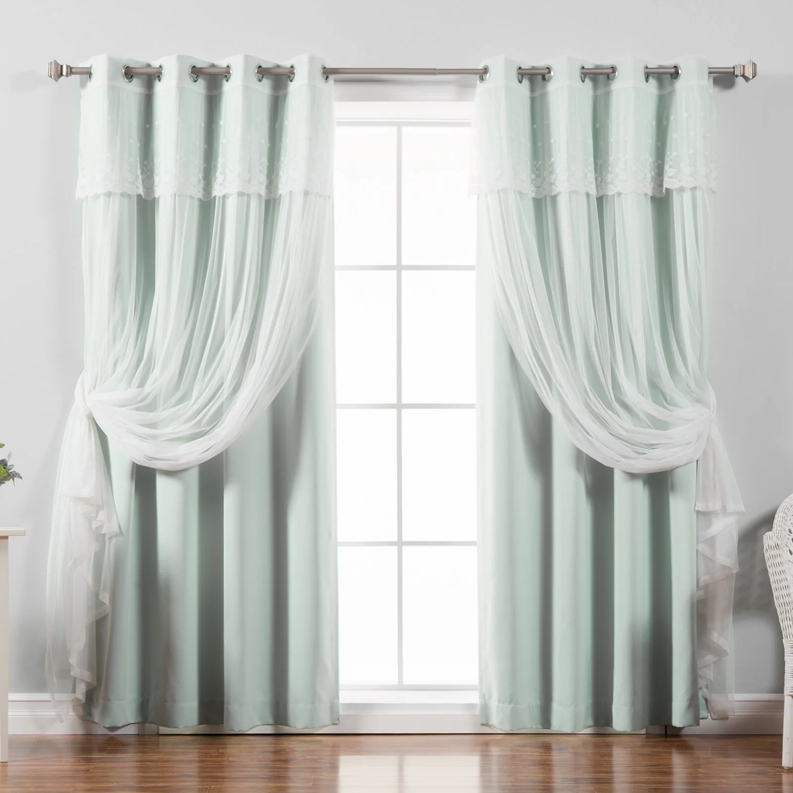 Layered mint green and sheer white lace curtains hang from a silver grommet rod on a grid window over wood floors.