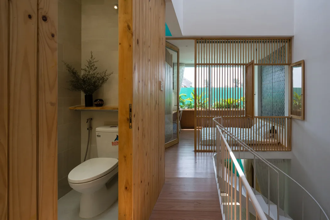 A minimalist residential hallway features a wood-slatted privacy screen next to a staircase and an open bathroom with a natural wood door.