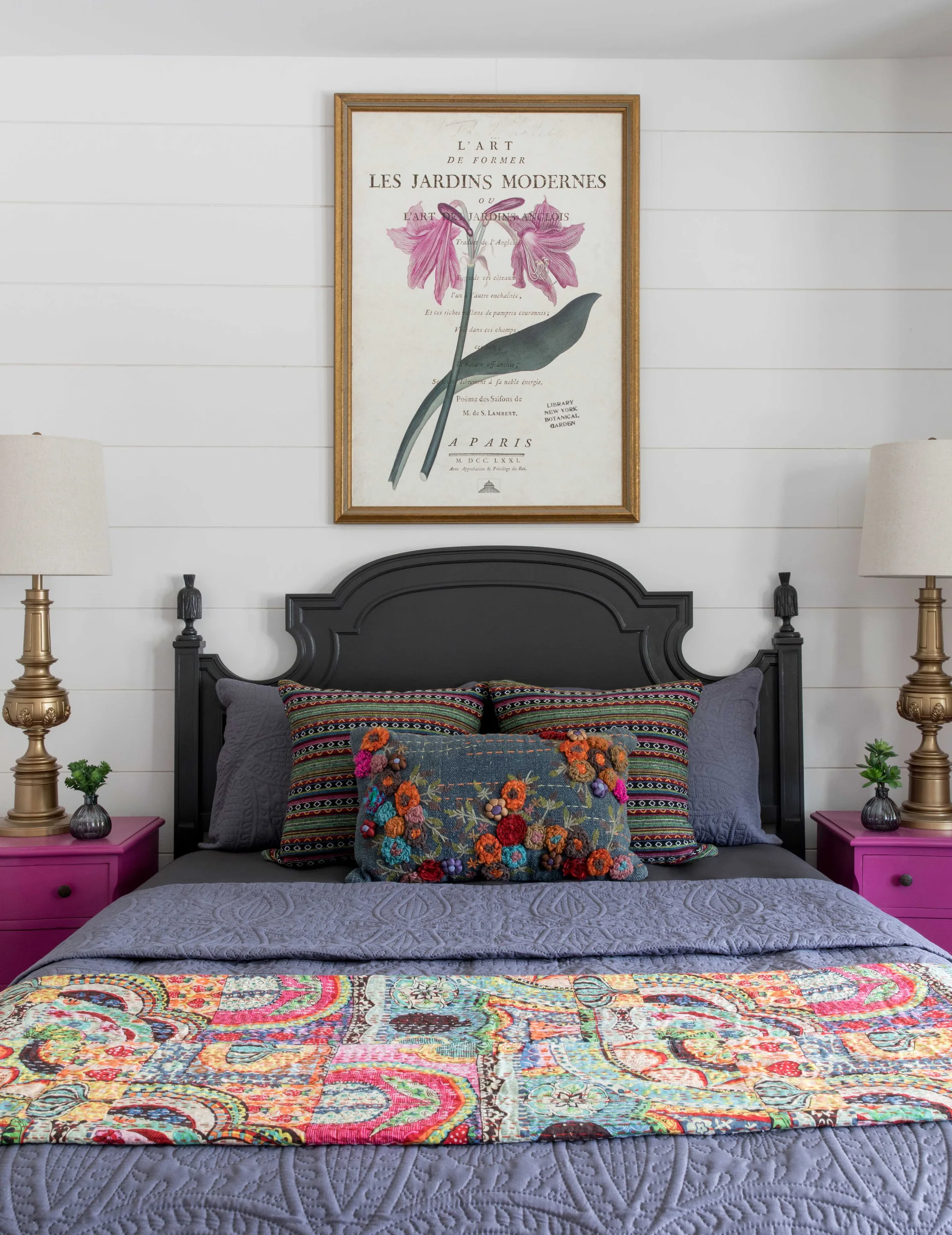 A symmetrical bedroom setup features a black headboard against white shiplap, flanked by magenta nightstands and brass lamps.