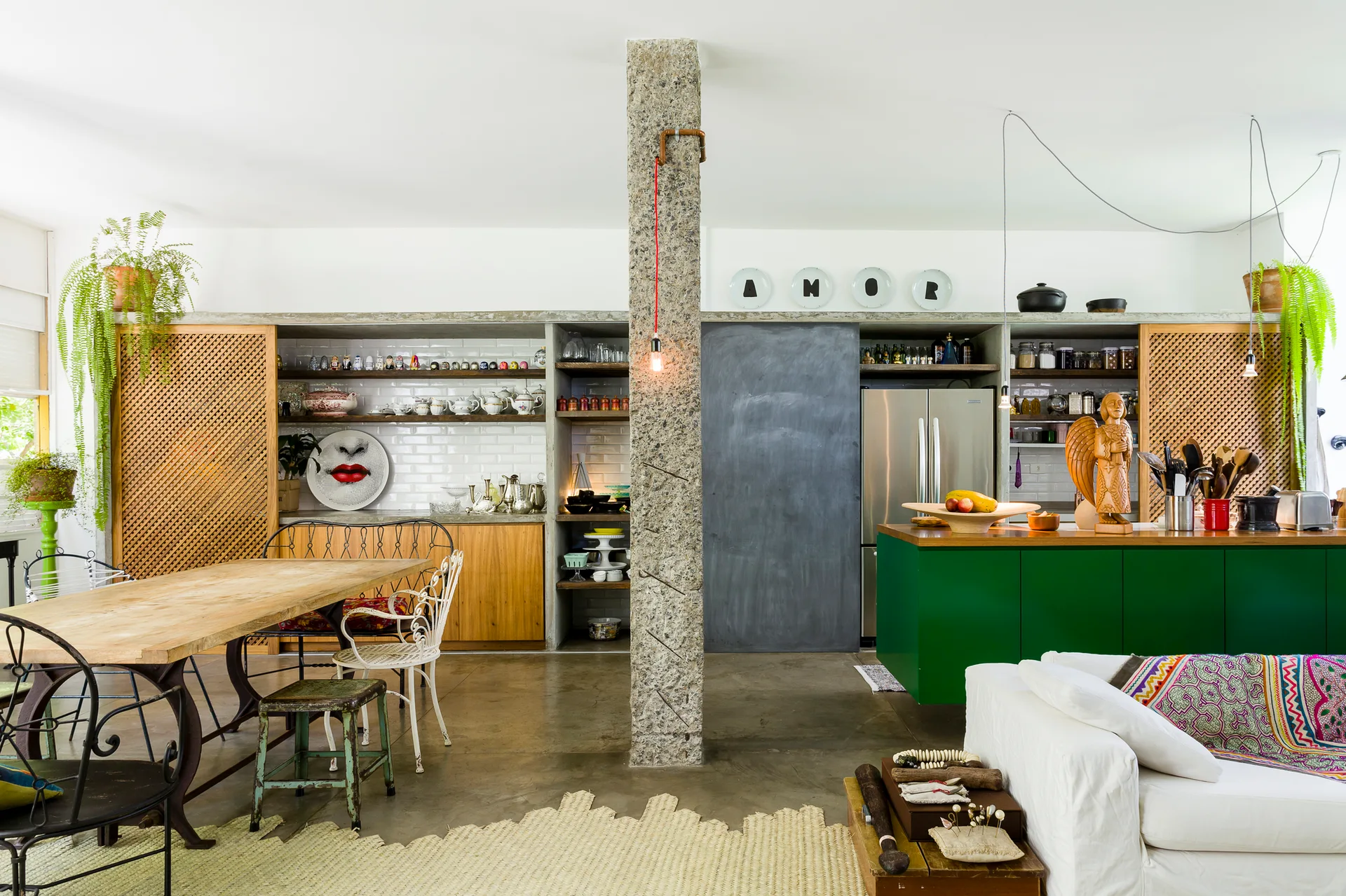 An open-plan kitchen and dining area featuring a green island, an exposed stone pillar, and a wooden dining table.