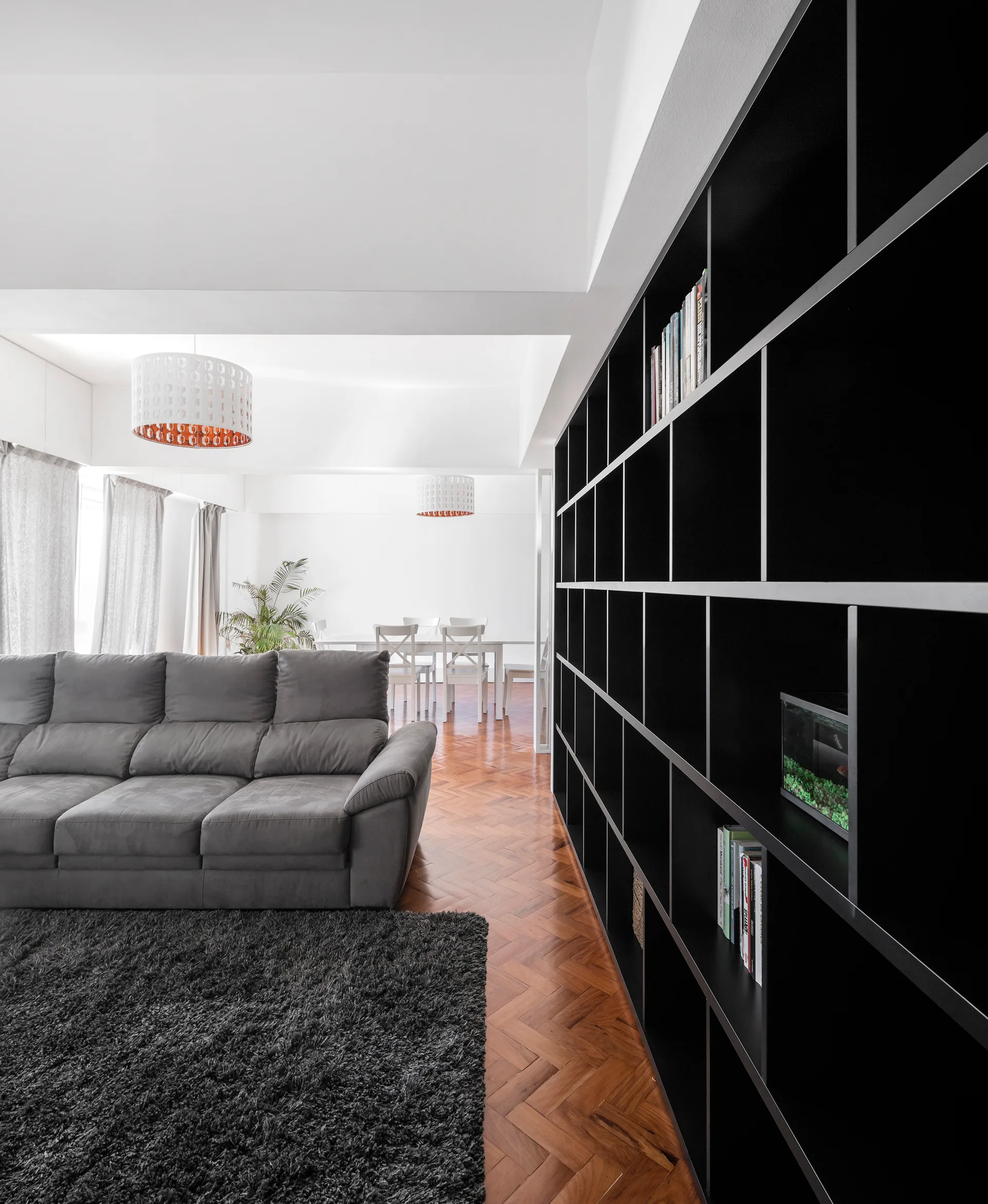 A spacious living room features a large black open bookshelf, a plush grey sofa on a shaggy rug, and warm wood herringbone parquet flooring.
