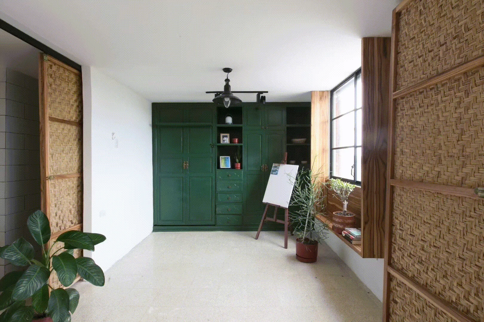 A bright room featuring a dark green built-in cabinetry unit, a wood-framed window, and textured woven sliding doors.
