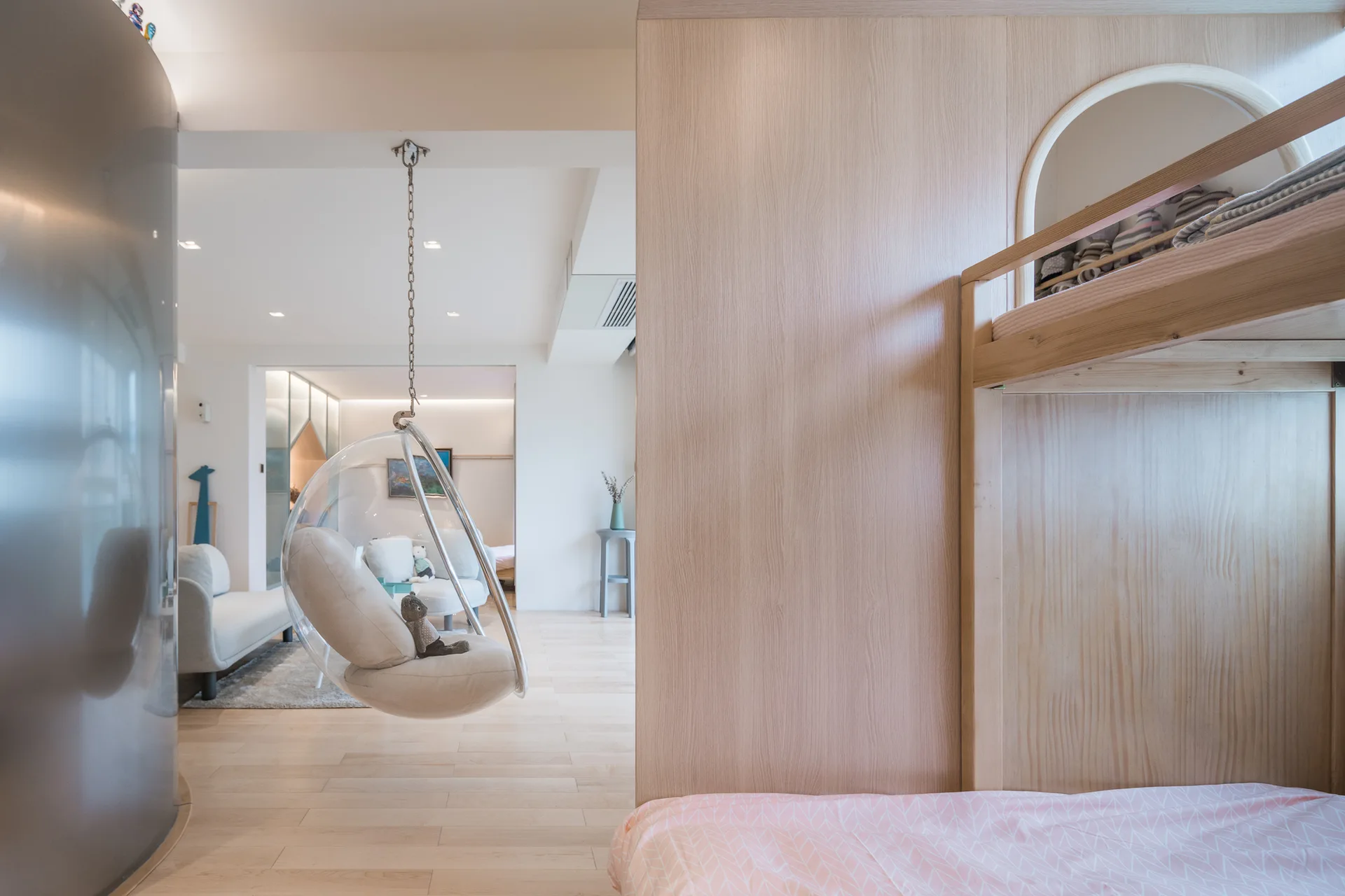 A light wood bunk bed partition stands next to a transparent hanging bubble chair in an open-concept playroom.