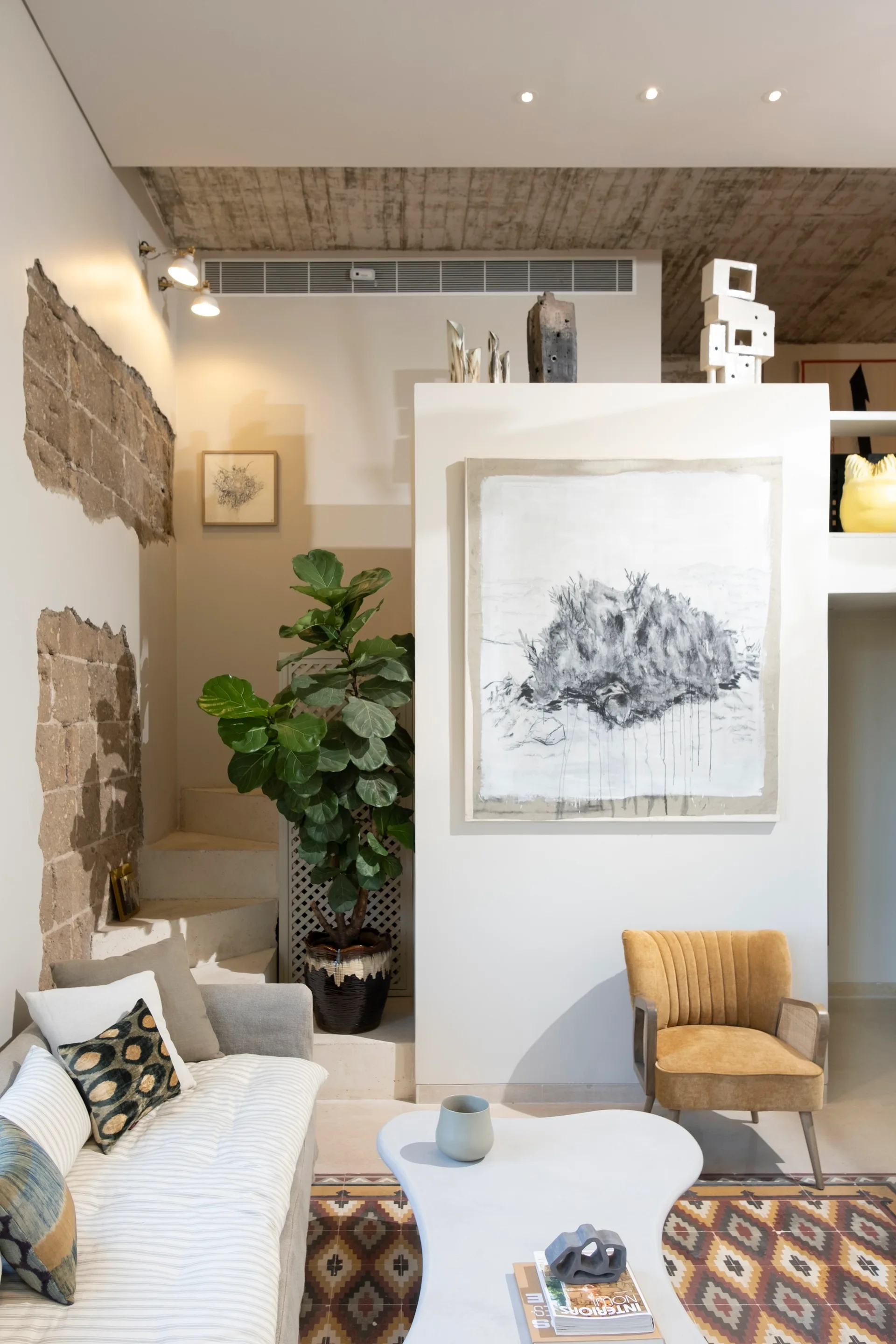 A living room with a grey sofa, an organic white coffee table, a mustard yellow velvet armchair, and an exposed raw stone accent wall.