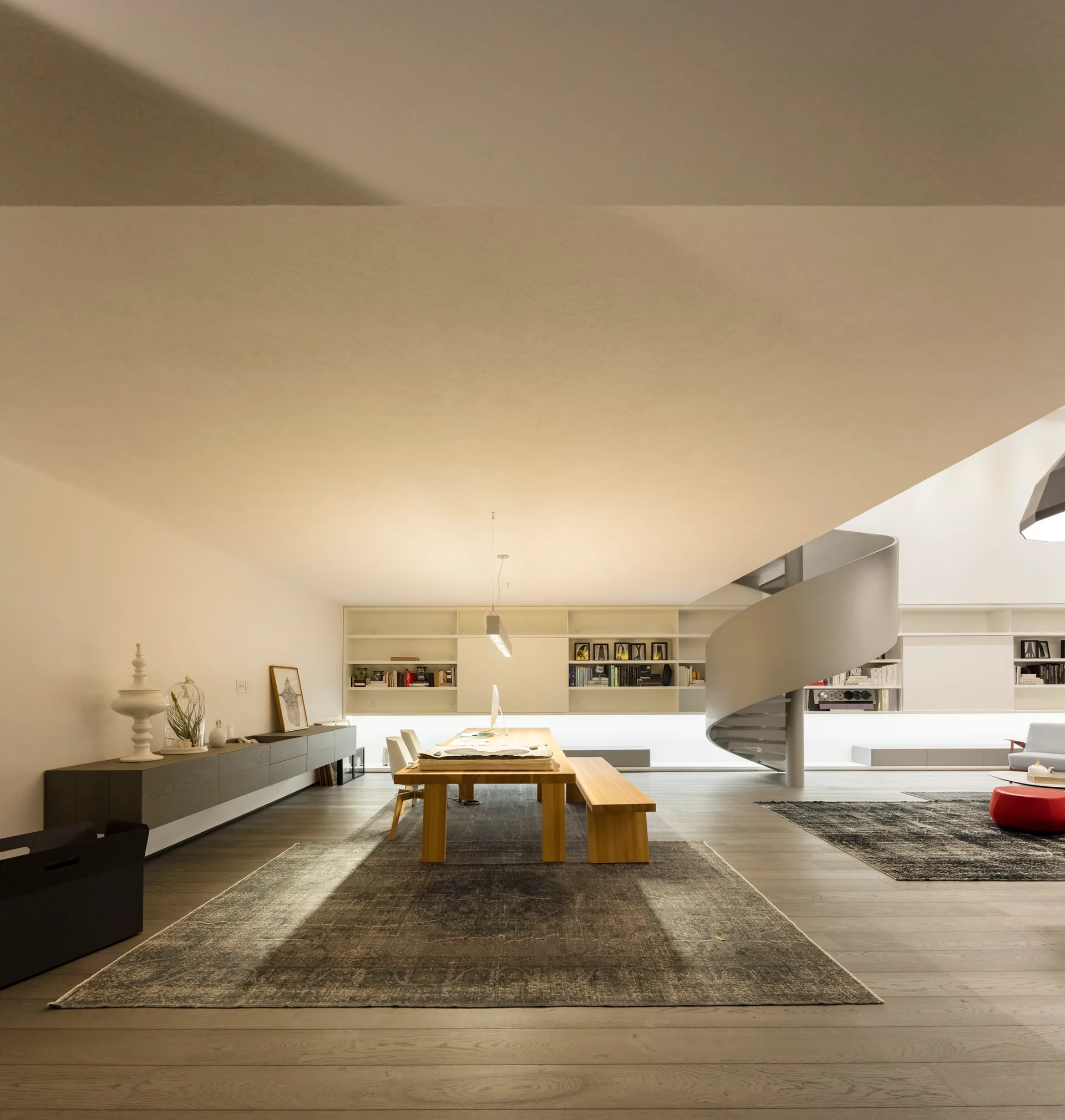 A spacious open-plan dining area features a wooden table and bench, a modern grey sideboard, and a prominent white spiral staircase.