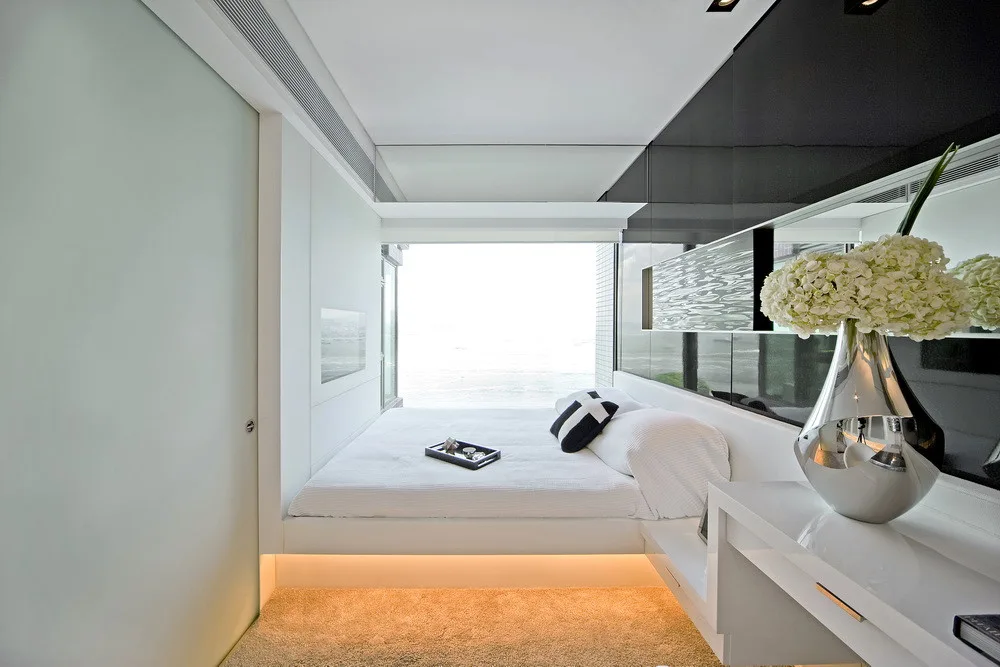A compact modern bedroom features a white built-in platform bed with integrated warm LED lighting underneath, set against high-gloss black wall panels.