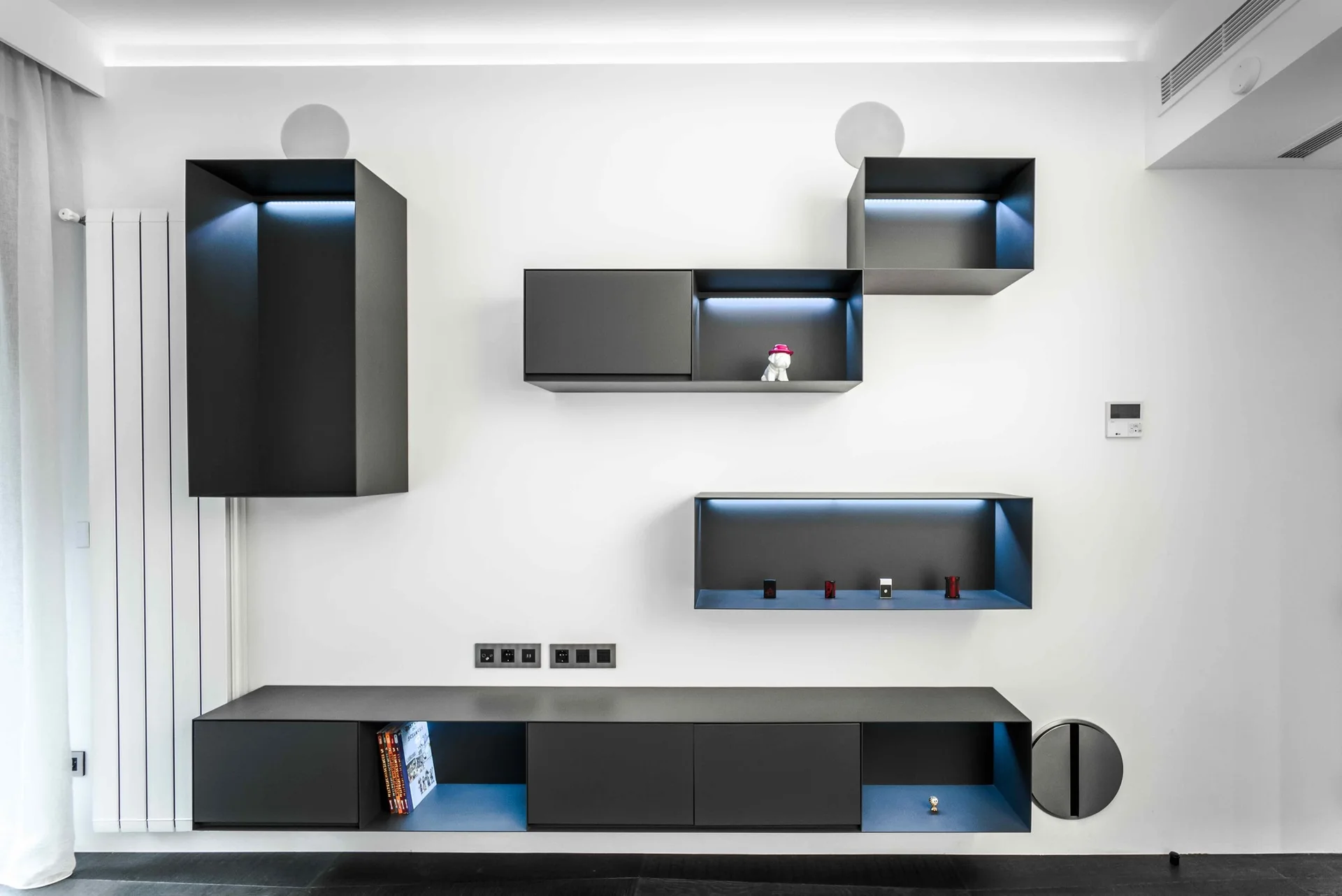 Matte black modular cabinets with cool blue LED lighting are mounted in an asymmetrical pattern on a white wall.
