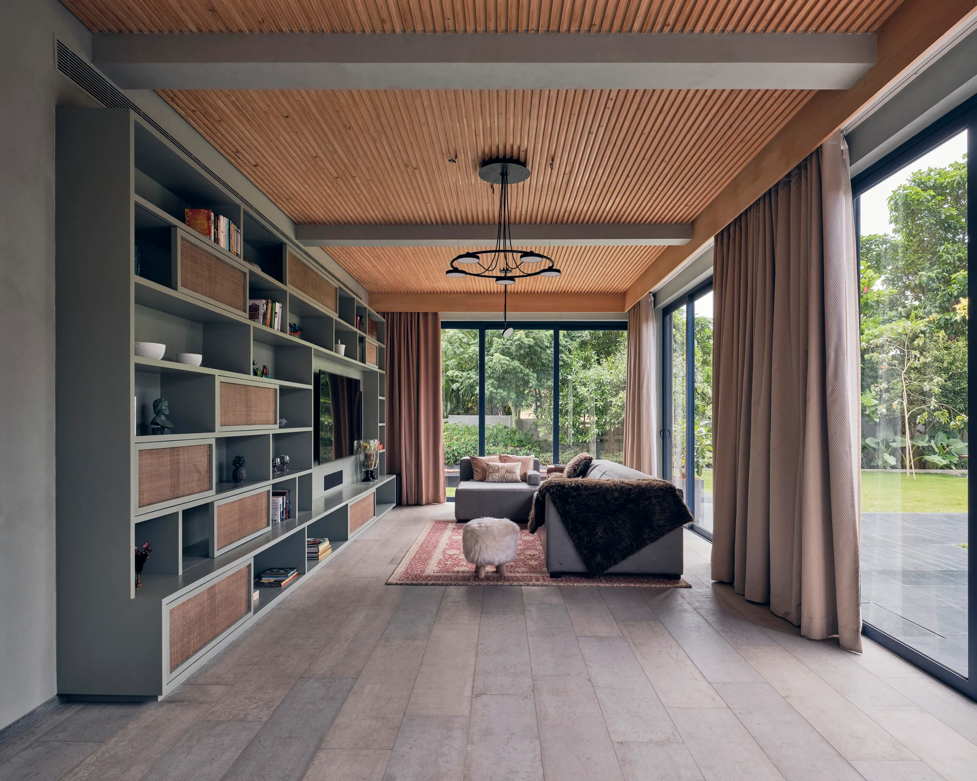 A contemporary living room featuring a large olive green shelving unit with cane doors, a wood slatted ceiling, and sliding glass doors to a garden.