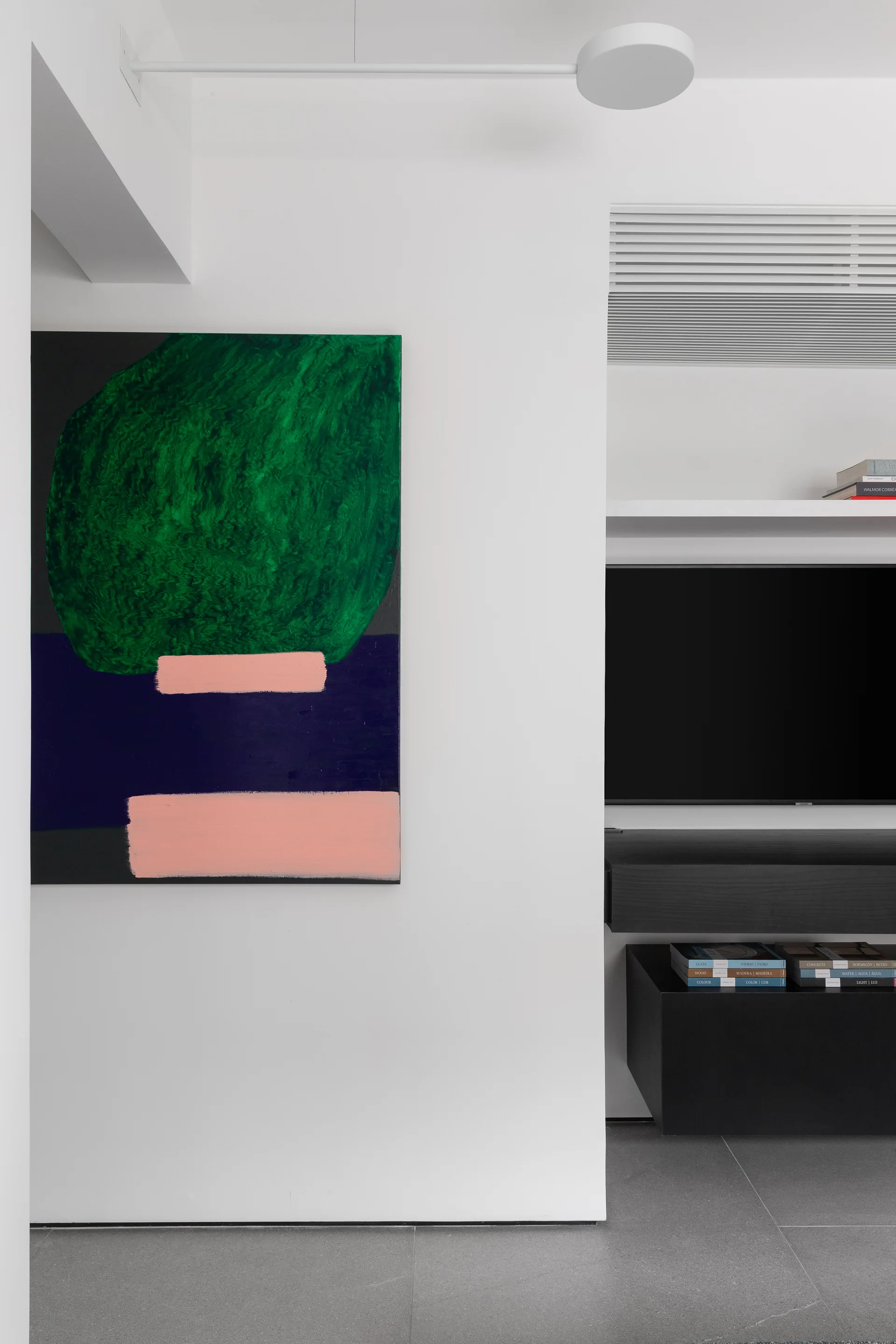 A large green and pink abstract painting hangs on a white wall next to a recessed media niche with a black TV and floating console.