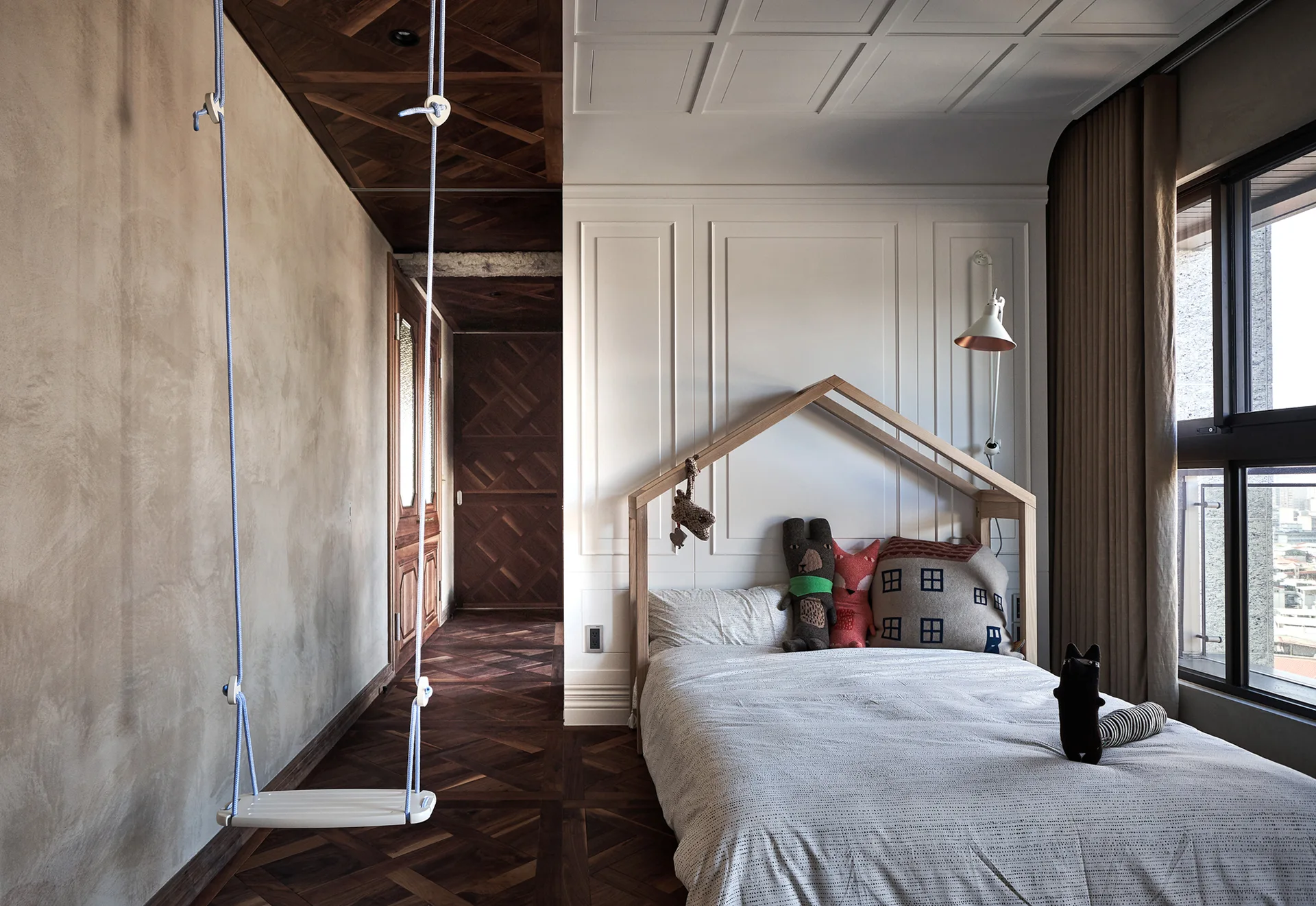 A child's bedroom with an indoor rope swing, a house-shaped bed frame with stuffed toys, and dark wood herringbone parquet floors.