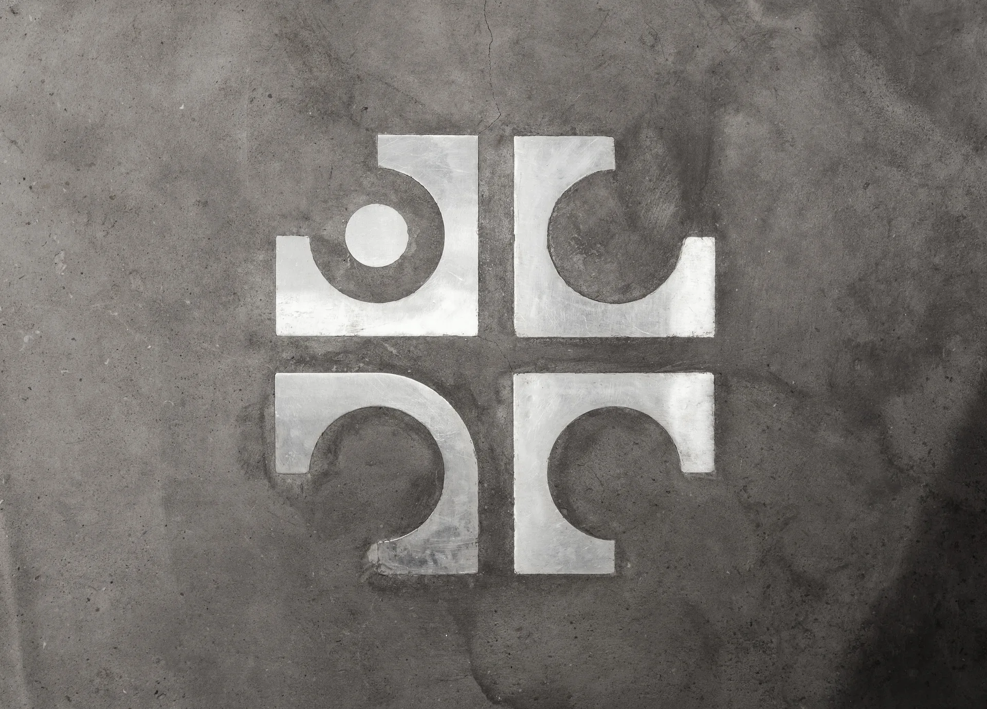 A close-up overhead view of a symmetrical geometric metal inlay embedded in a grey concrete floor.