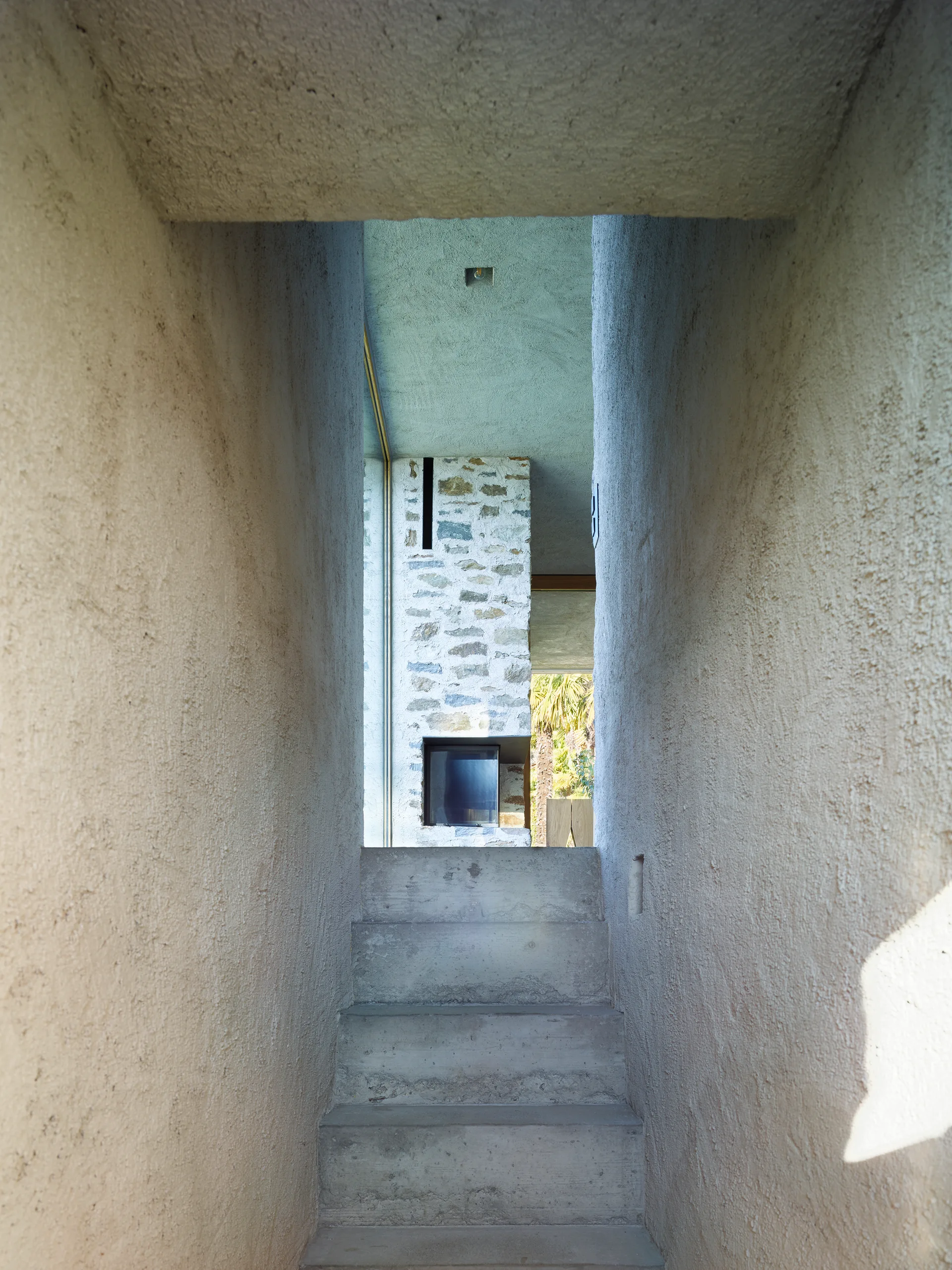 A narrow staircase corridor with rough stucco walls and concrete steps leading to a modern stone fireplace structure.