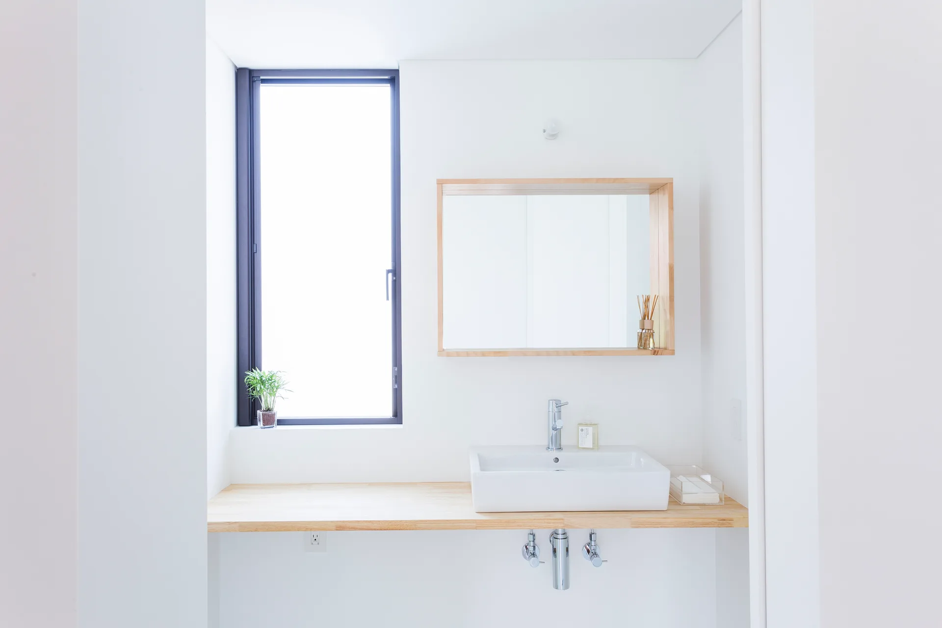 A minimalist bathroom vanity featuring a floating light wood countertop, a white vessel sink, and a wood-framed mirror set against a white wall.