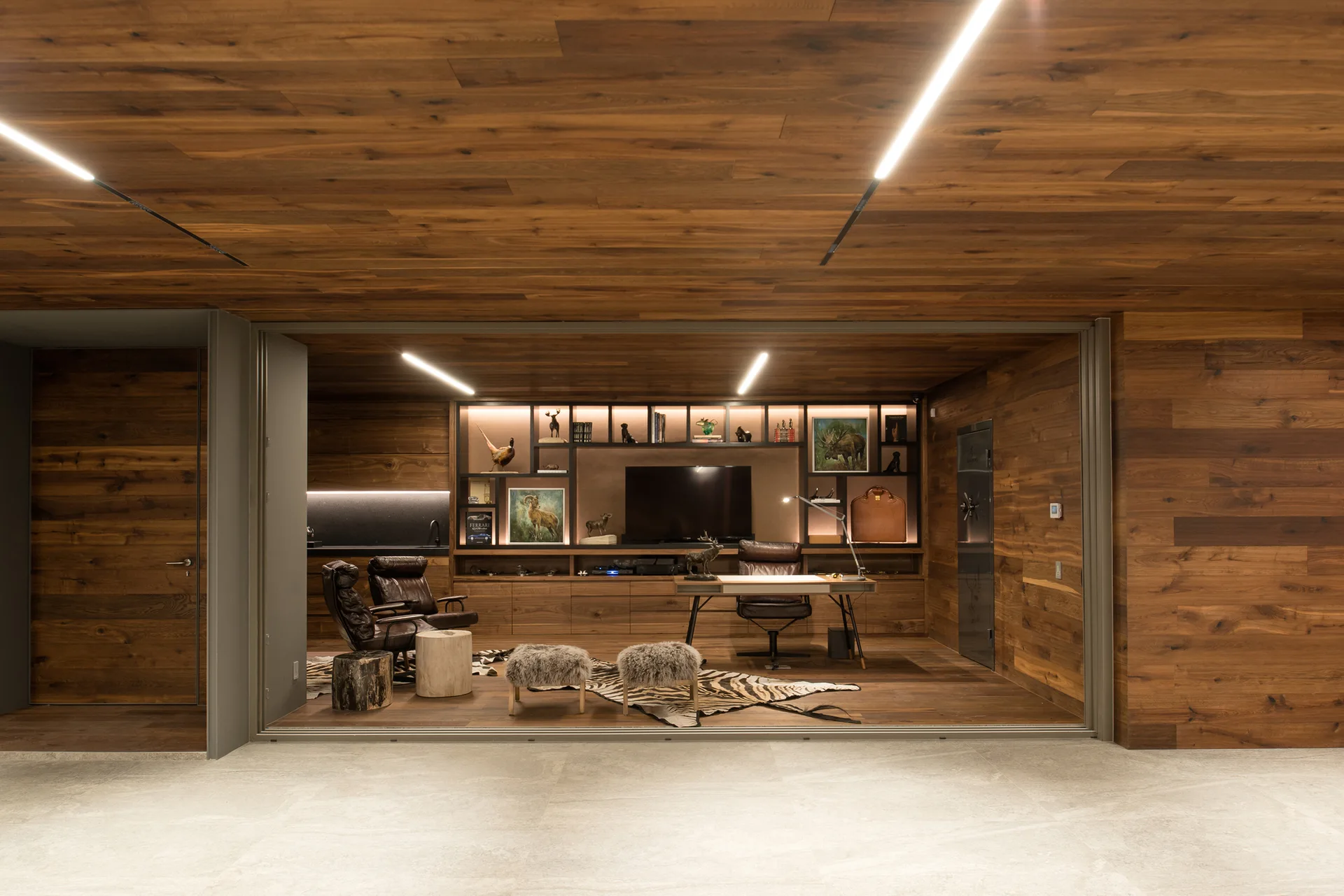 A modern home office with wood plank walls and ceiling, a dark wood desk with leather chairs, and built-in shelving.