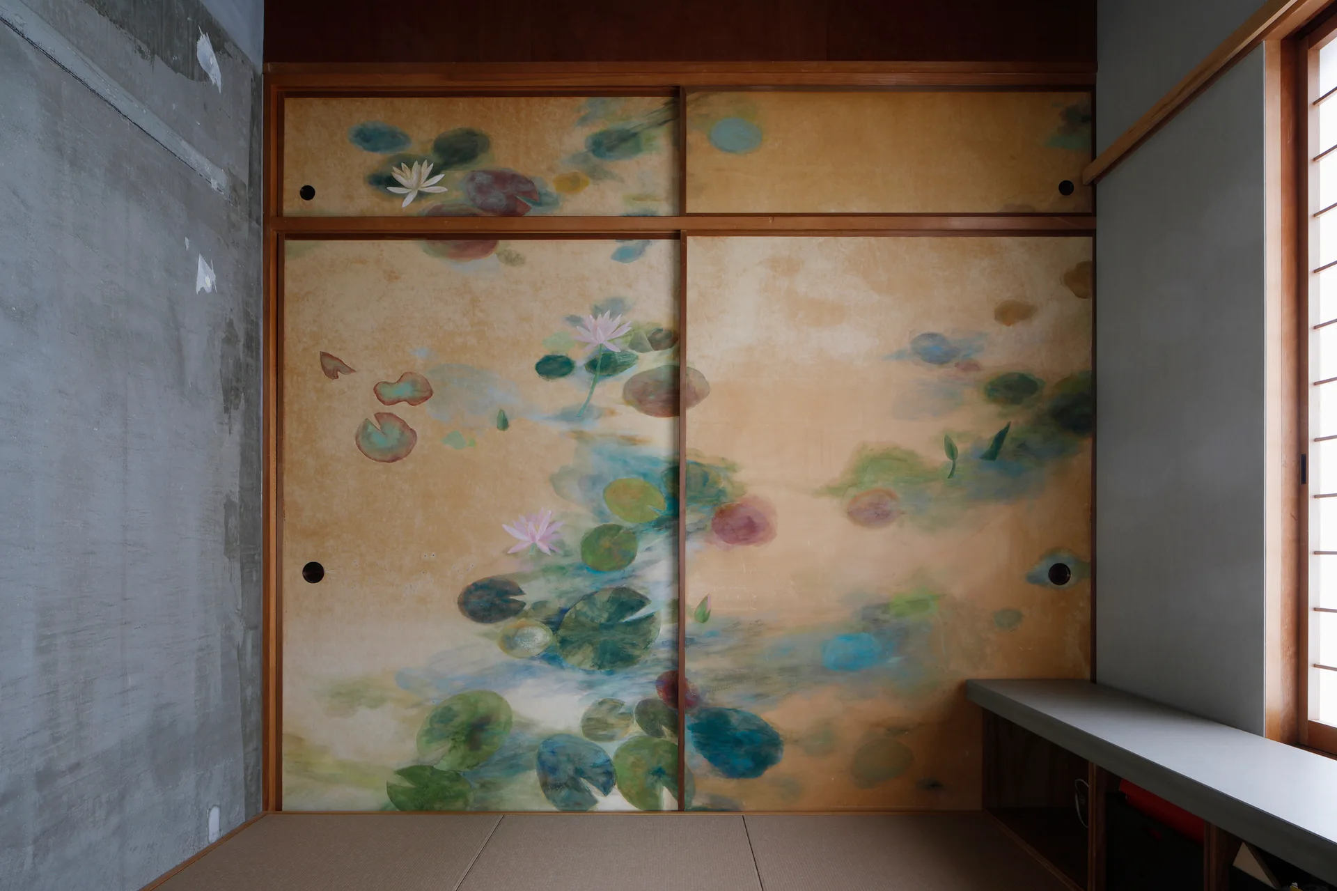 A Japanese minimalist room featuring painted lotus sliding doors, a raw concrete wall, and woven tatami floor mats.