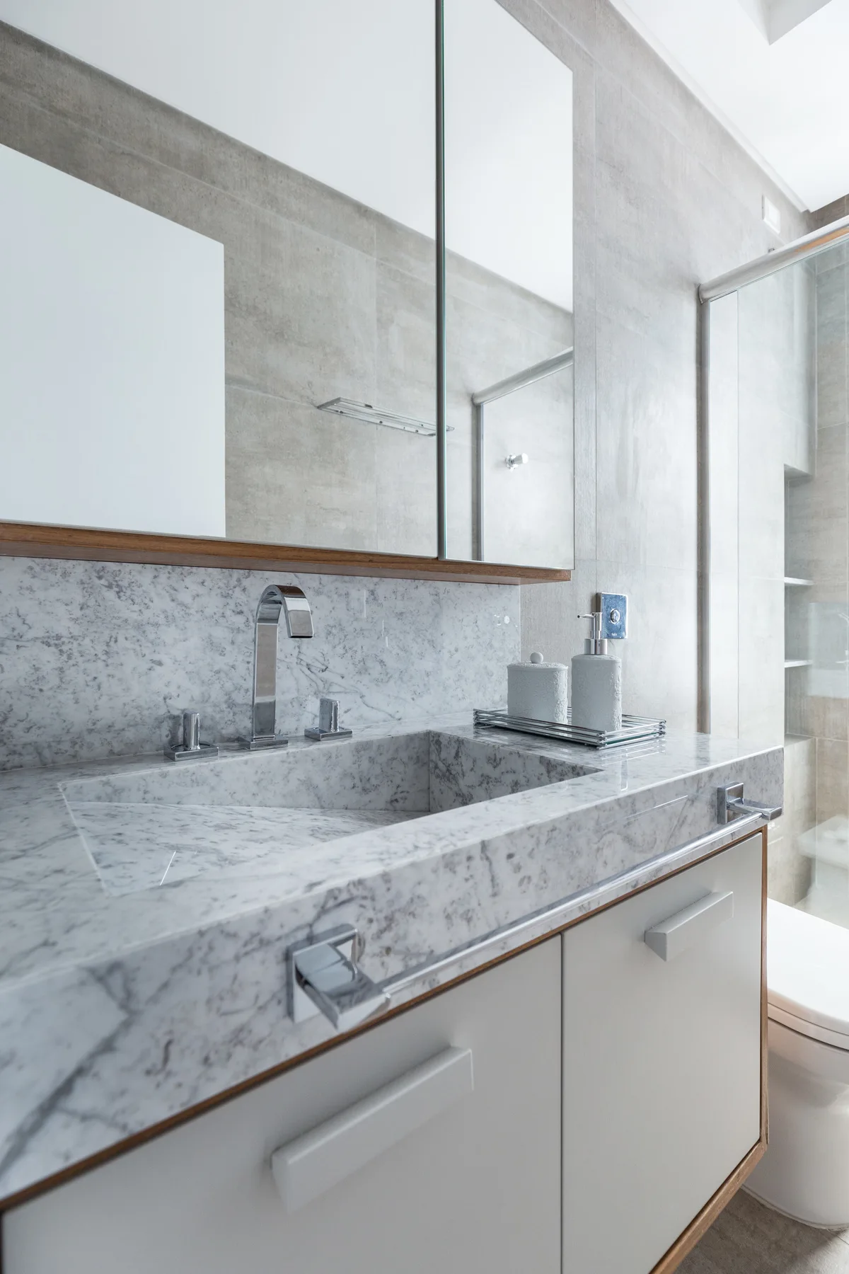 A close-up of a modern bathroom vanity featuring an integrated veined marble sink with a chrome faucet below a mirrored cabinet.