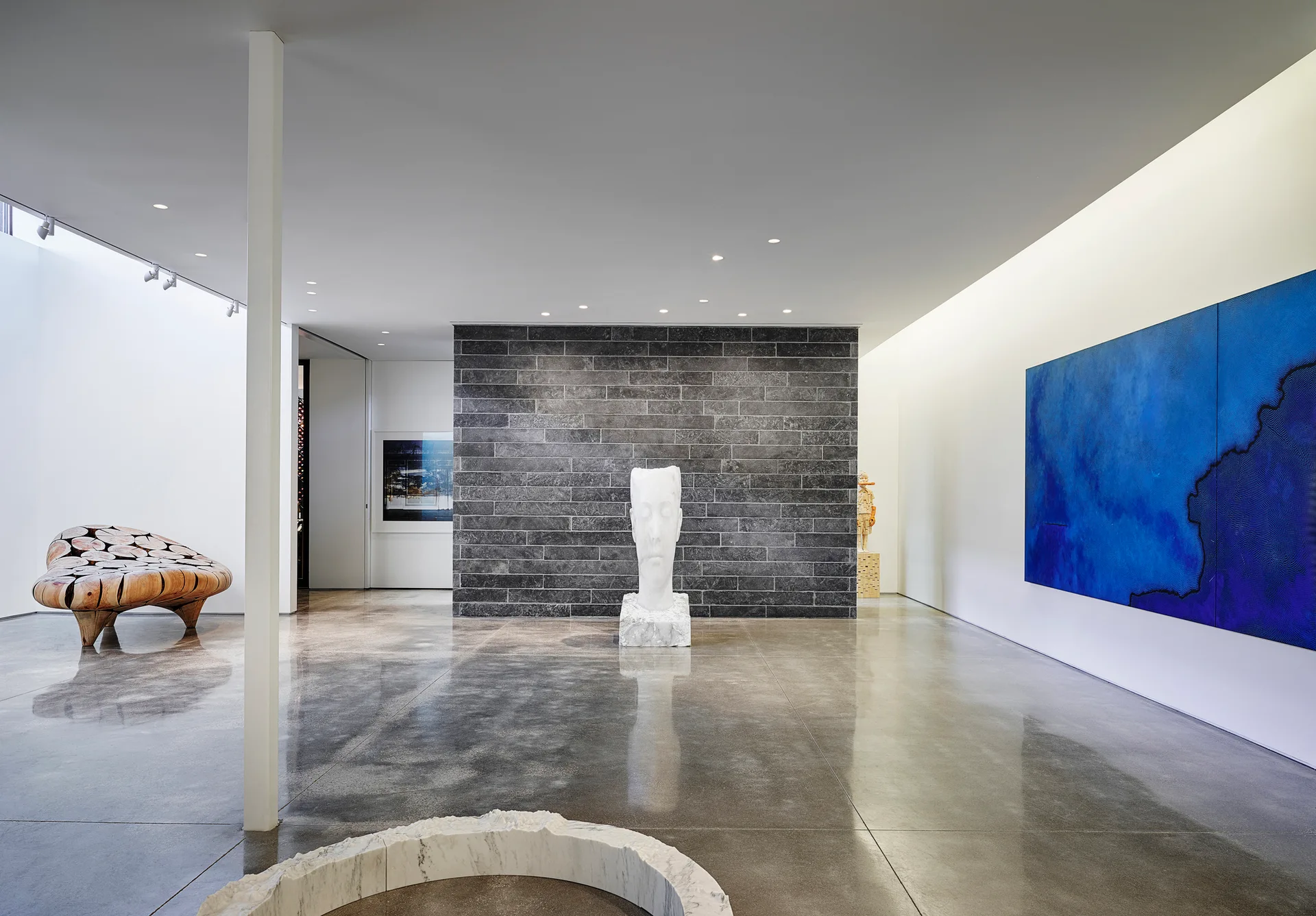 A spacious minimalist gallery featuring a dark gray stone feature wall, highly reflective polished concrete floors, and sculptural art.