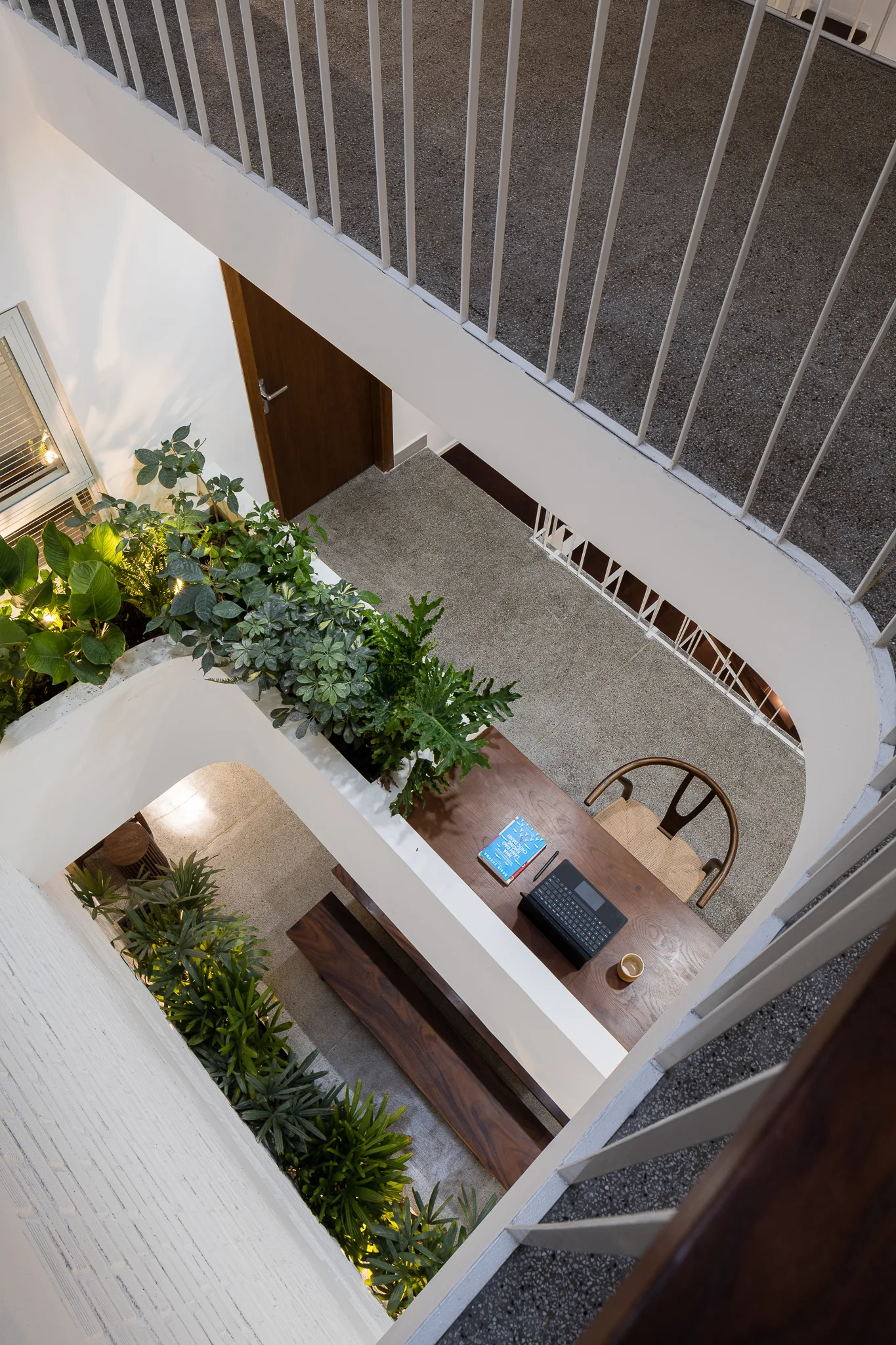 A high-angle view of a modern stairwell landing featuring a built-in wooden desk with a wishbone chair, wood bench, and integrated green planters.